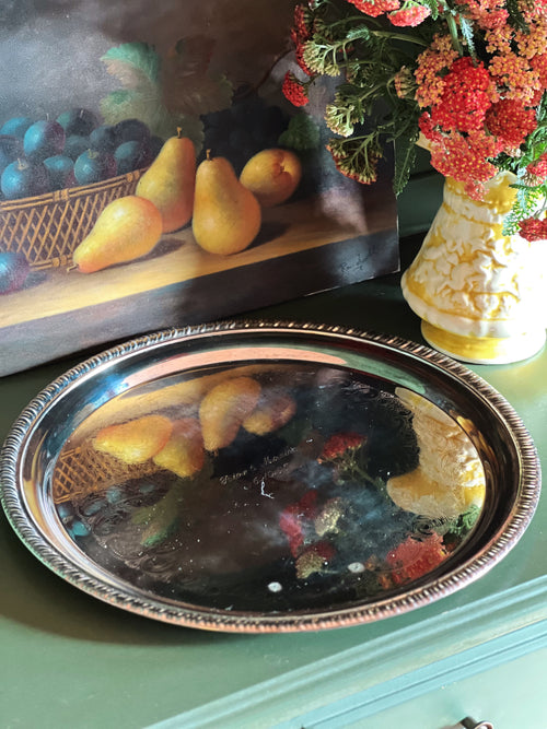 Decorative tray with fruit design, painting of pears, and vase with flowers on a green surface.