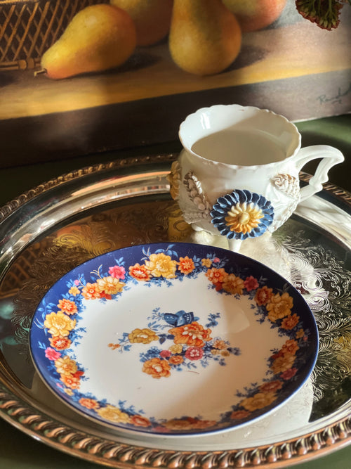 Decorative ceramic plate with floral design on a silver tray, accompanied by a decorative pitcher.