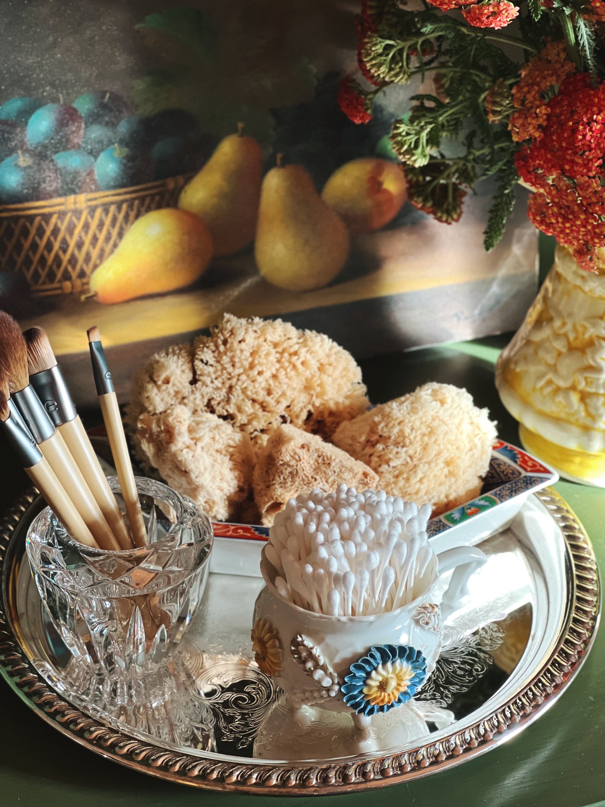 Decorative still life with sponges, brushes, and a vase on a reflective surface.