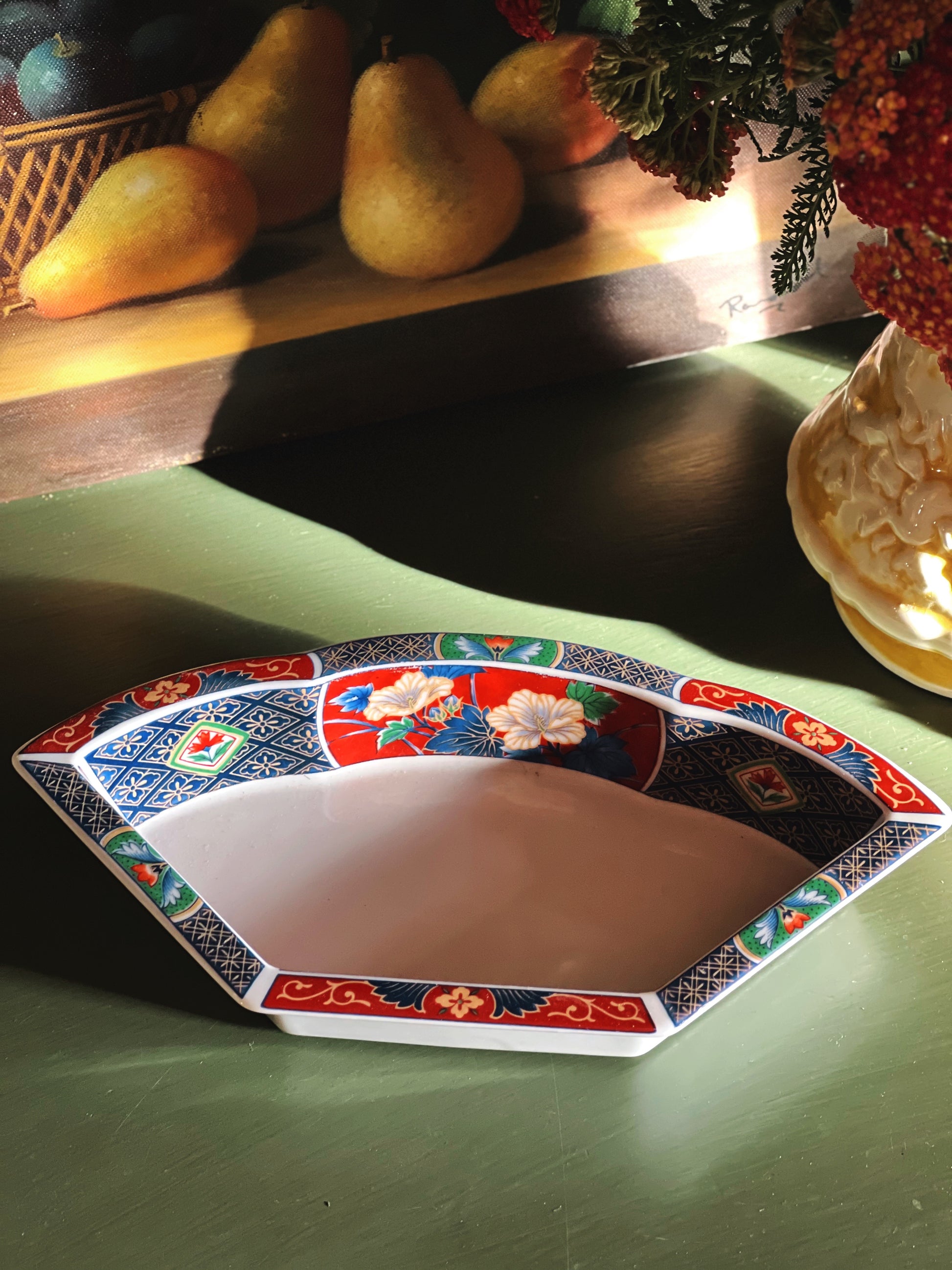 Decorative ceramic plate with floral patterns on a green surface, with pears and flowers in the background.
