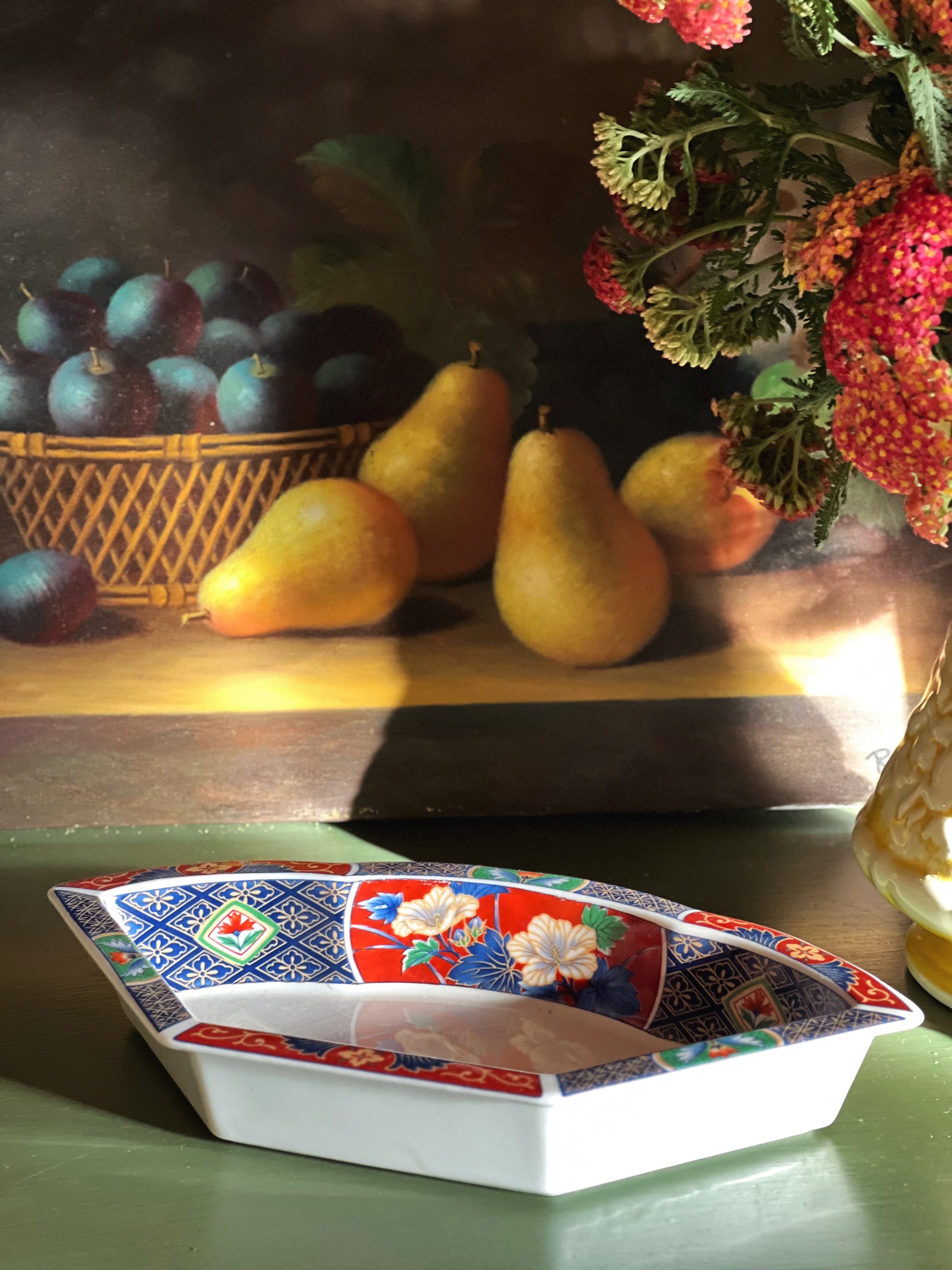 Decorative bowl with floral patterns on a table with fruits and flowers in the background