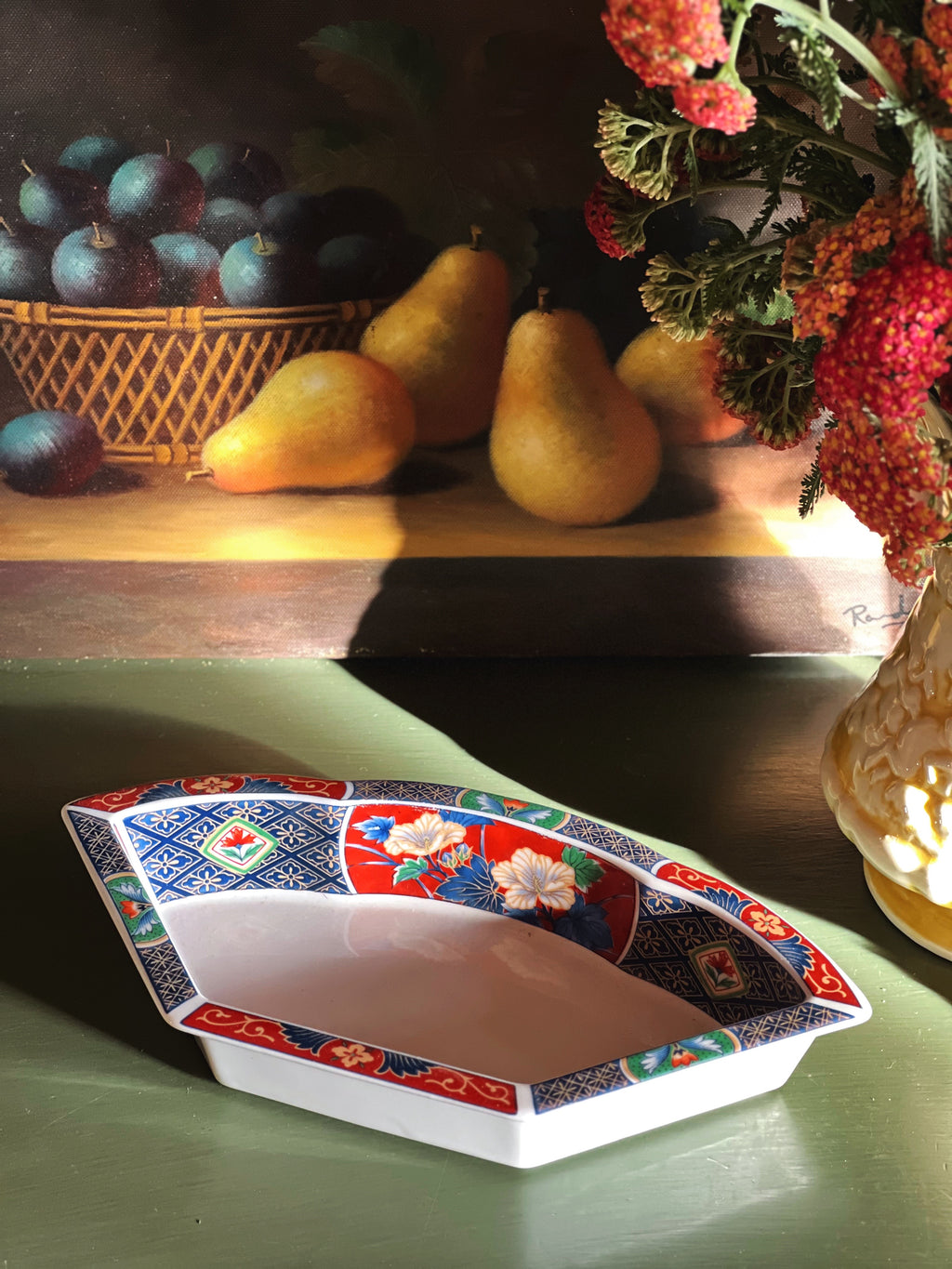 Decorative ceramic dish with floral patterns on a table with fruits and flowers in the background