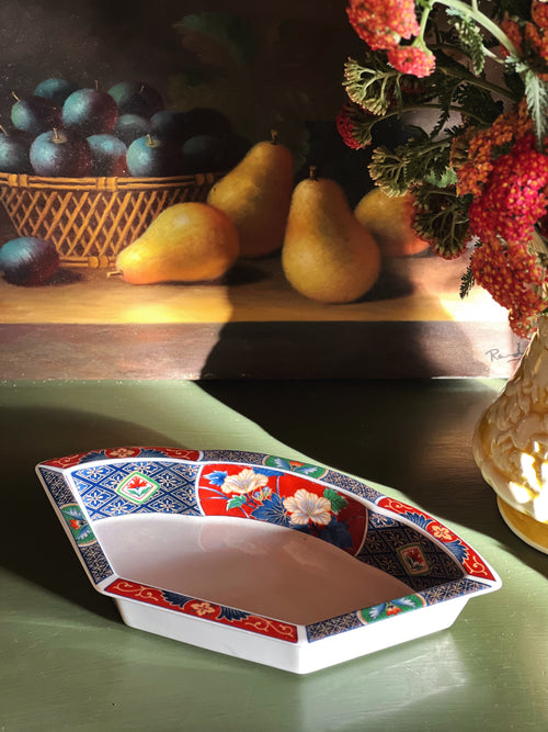 Decorative ceramic dish with floral patterns on a table with fruits and flowers in the background