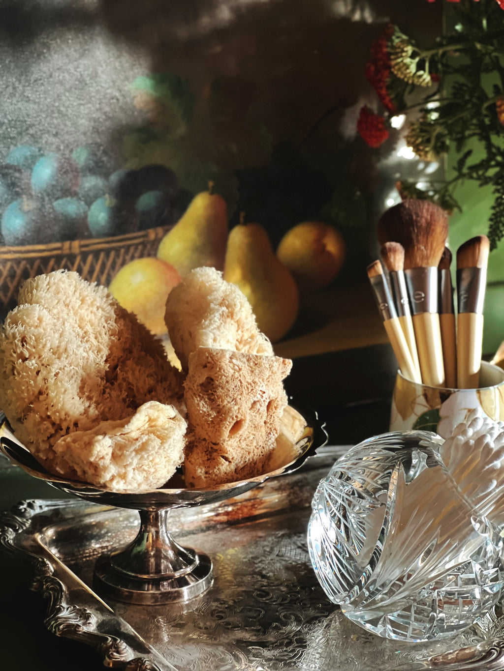 Sponges on a silver dish with pears and makeup brushes in the background