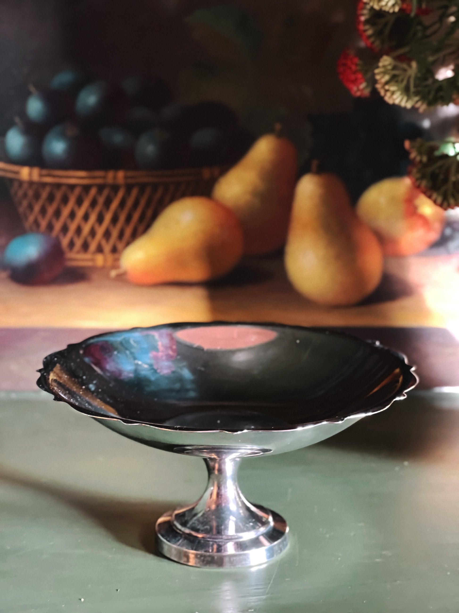 Silver footed dish on a table with fruits in the background
