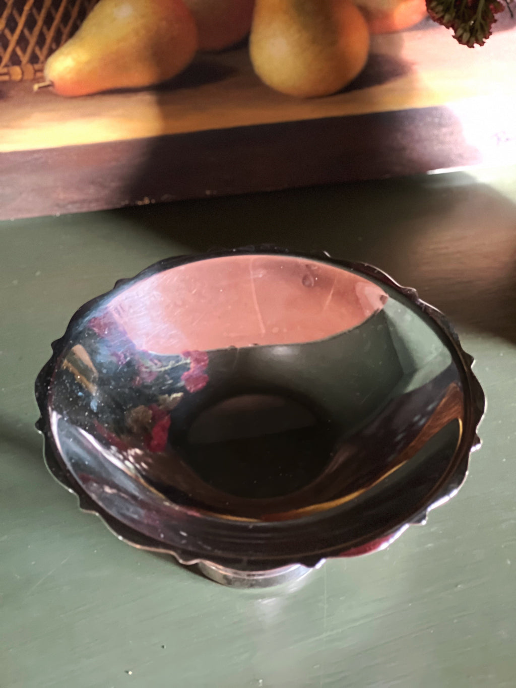 Decorative metal bowl on a green surface with fruits in the background