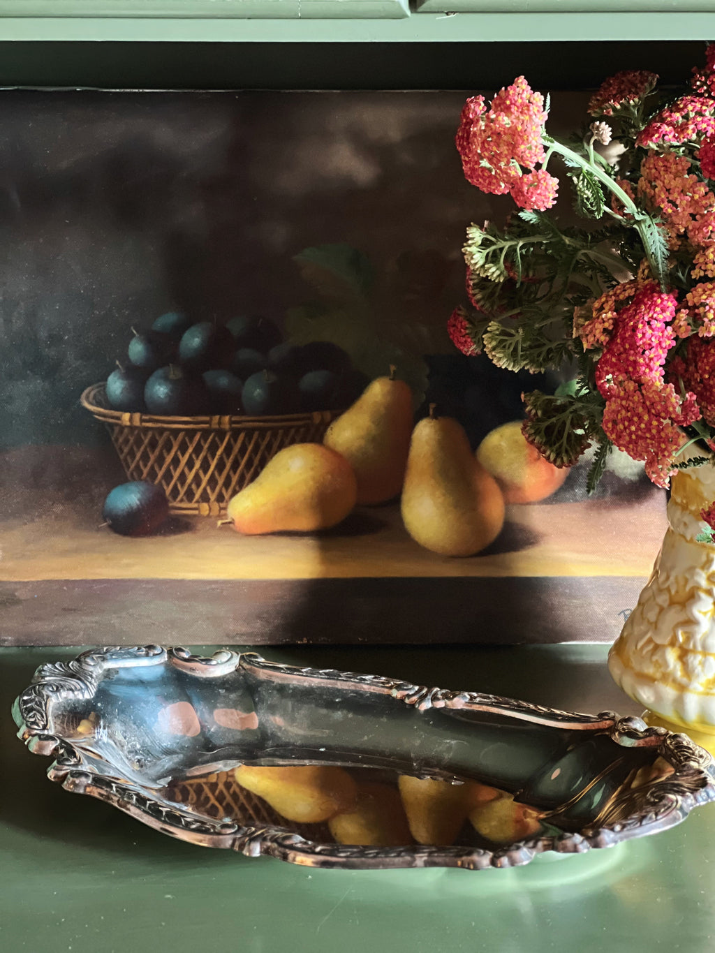 Still life arrangement with fruits and flowers and a silver bowl on a wooden surface.