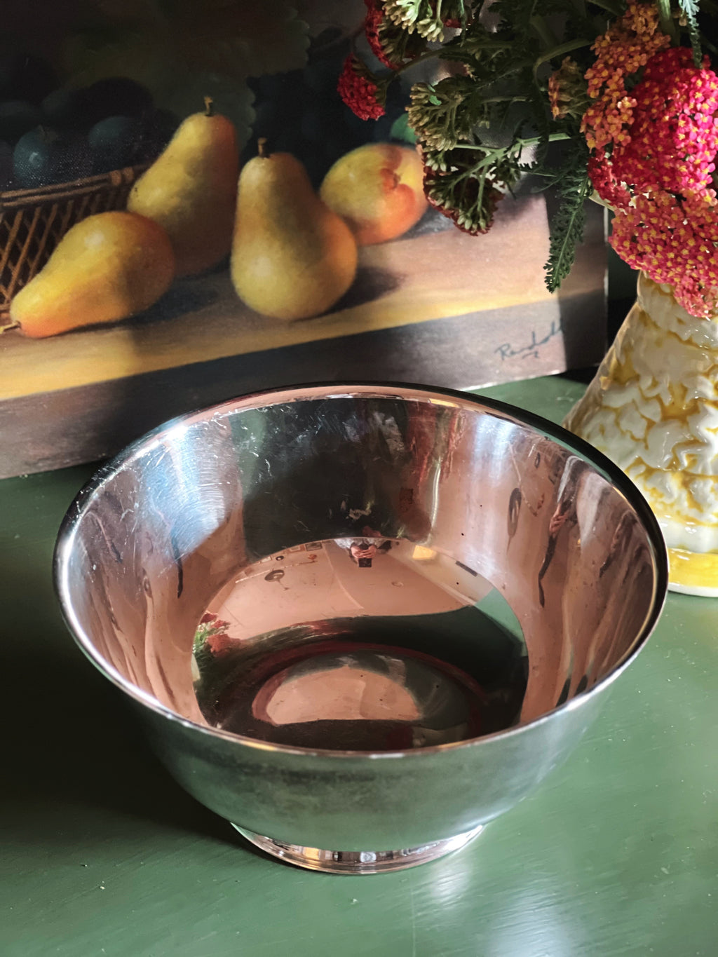 Overhead view of a silver Paul Revere bowl on a green surface with pears and flowers in the background