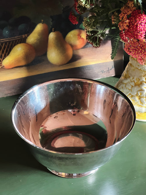 Overhead view of a silver Paul Revere bowl on a green surface with pears and flowers in the background
