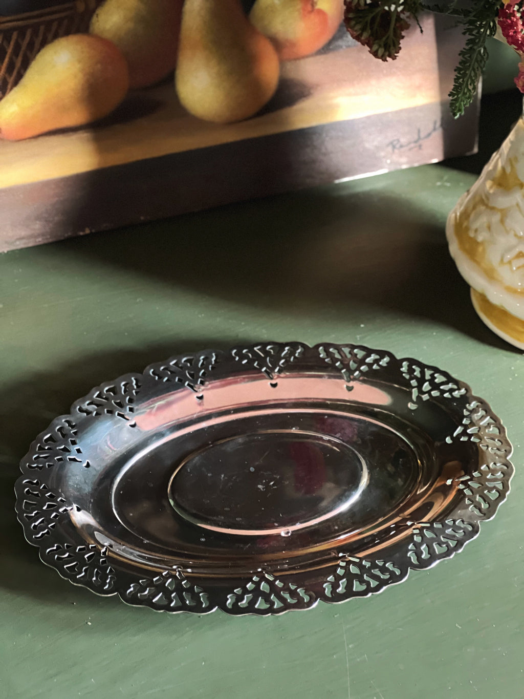 Decorative silver platter on a green surface with fruit in the background