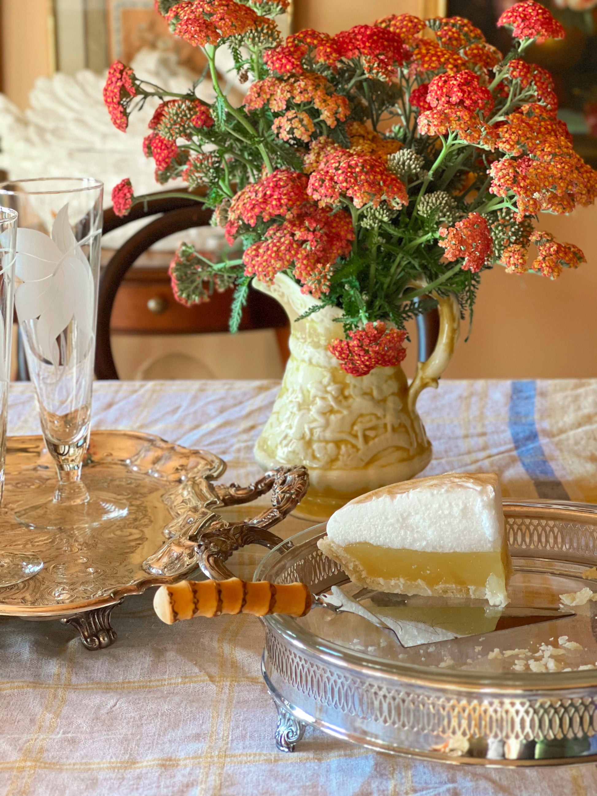 Bouquet of red flowers in a decorative vase on a table with a slice of pie and a glass.