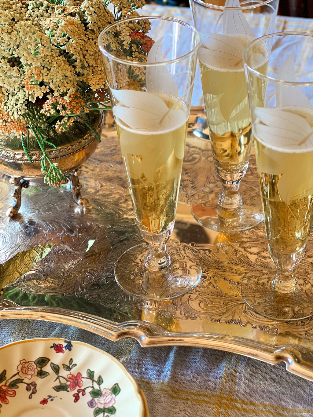 Set of four vintage etched floral champagne flutes filled with sparkling wine on a silver tray.