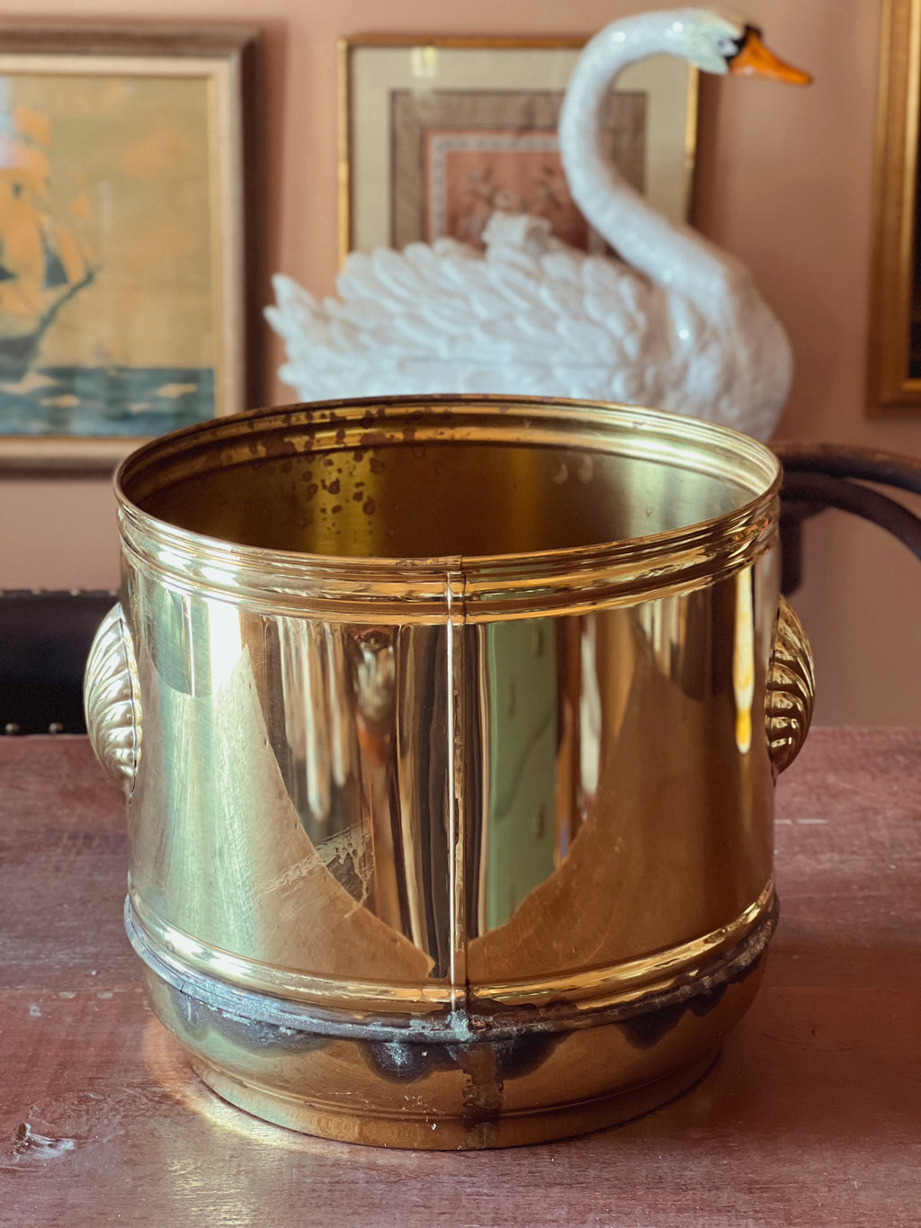 Gold-colored container on a surface with a decorative swan and framed pictures in the background.