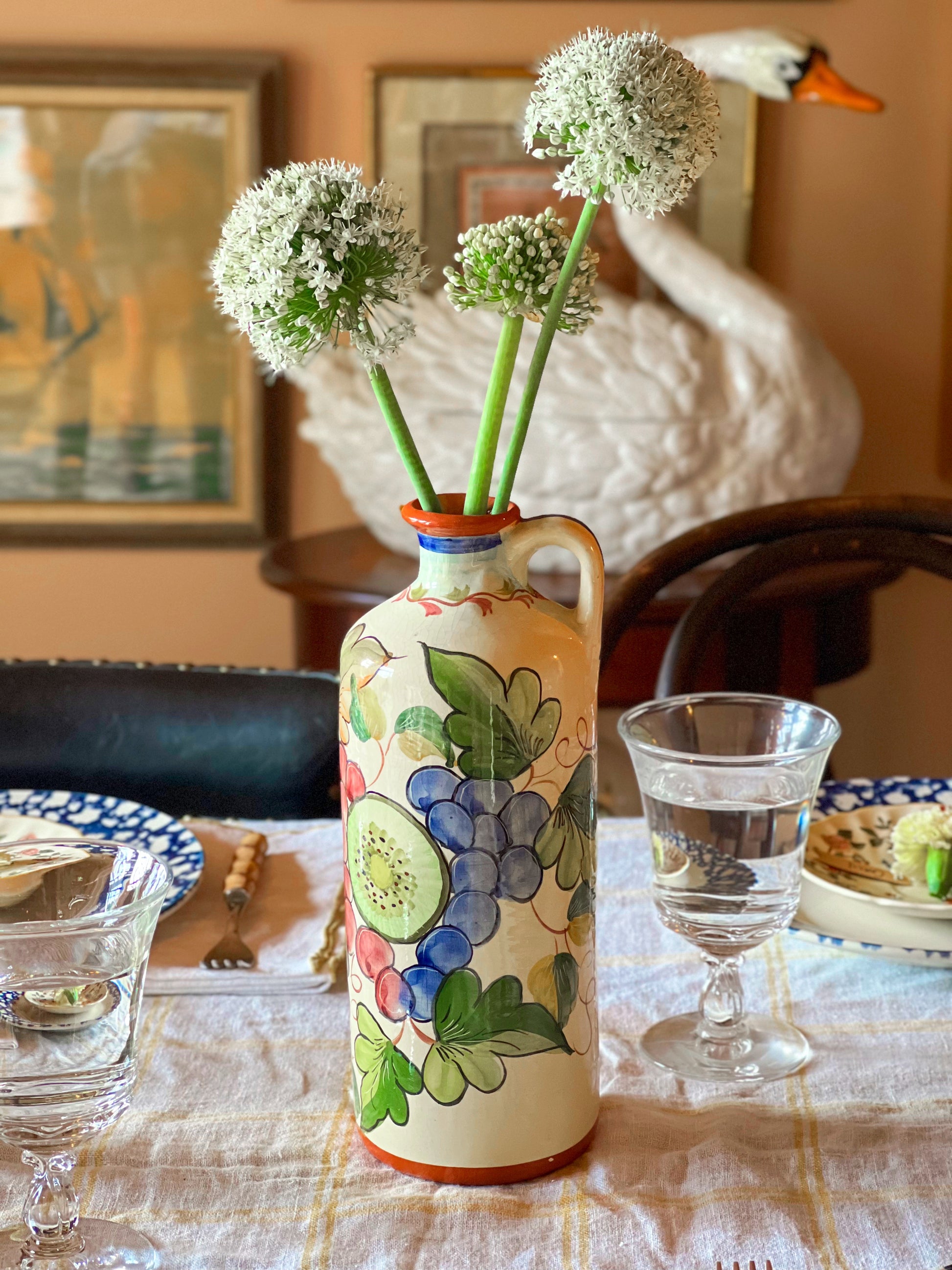 Decorative vase with floral design on a table with a swan sculpture in the background.