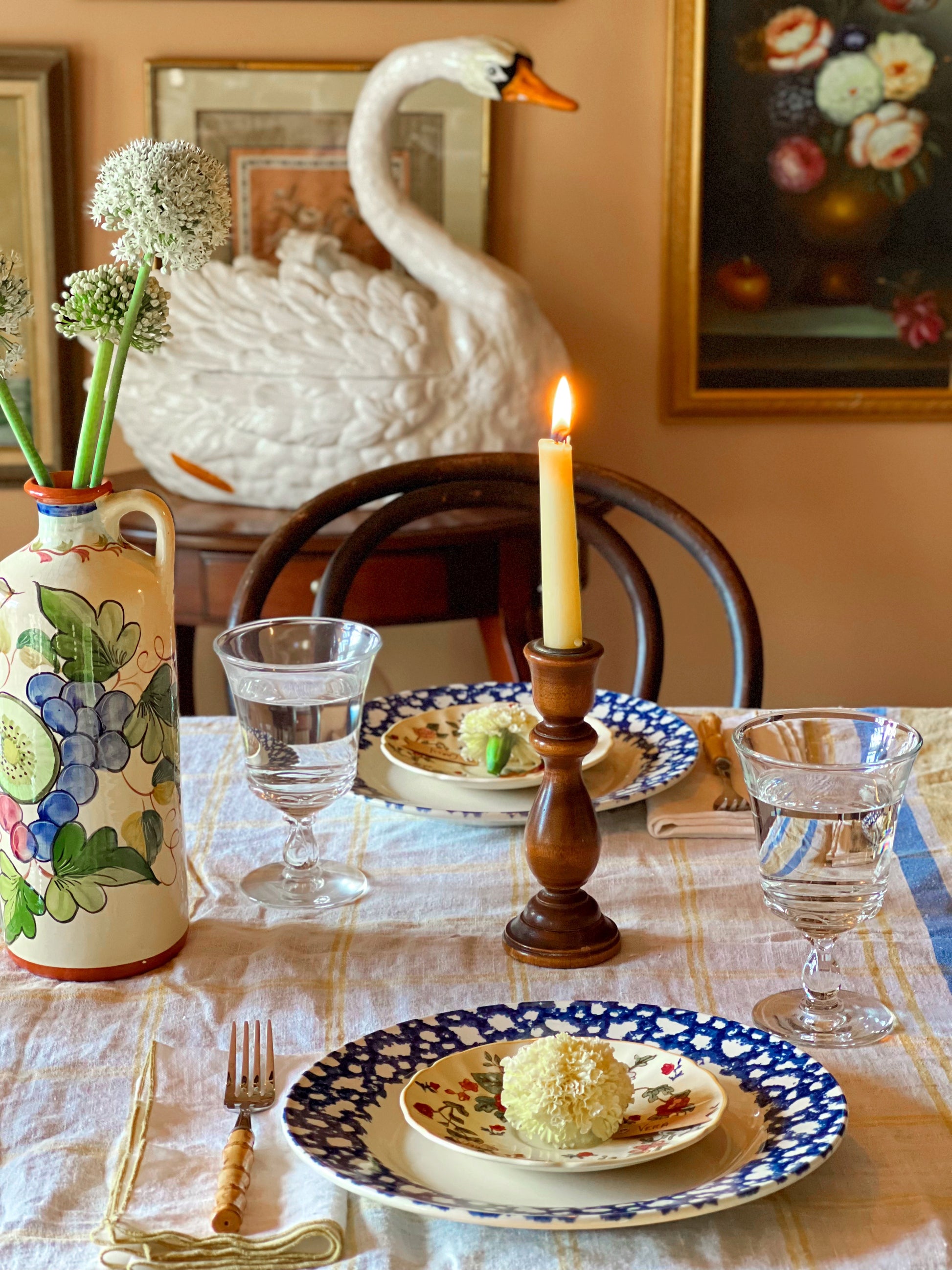 Dining table set with plates, glasses, and a candle, featuring a decorative swan tureen.