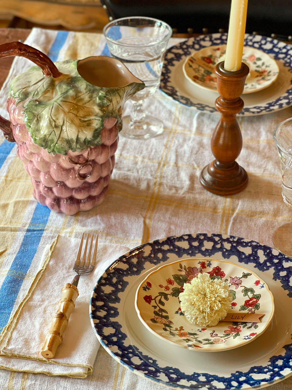 Decorative table setting with grape-shaped pitcher, floral plates, and candlestick.