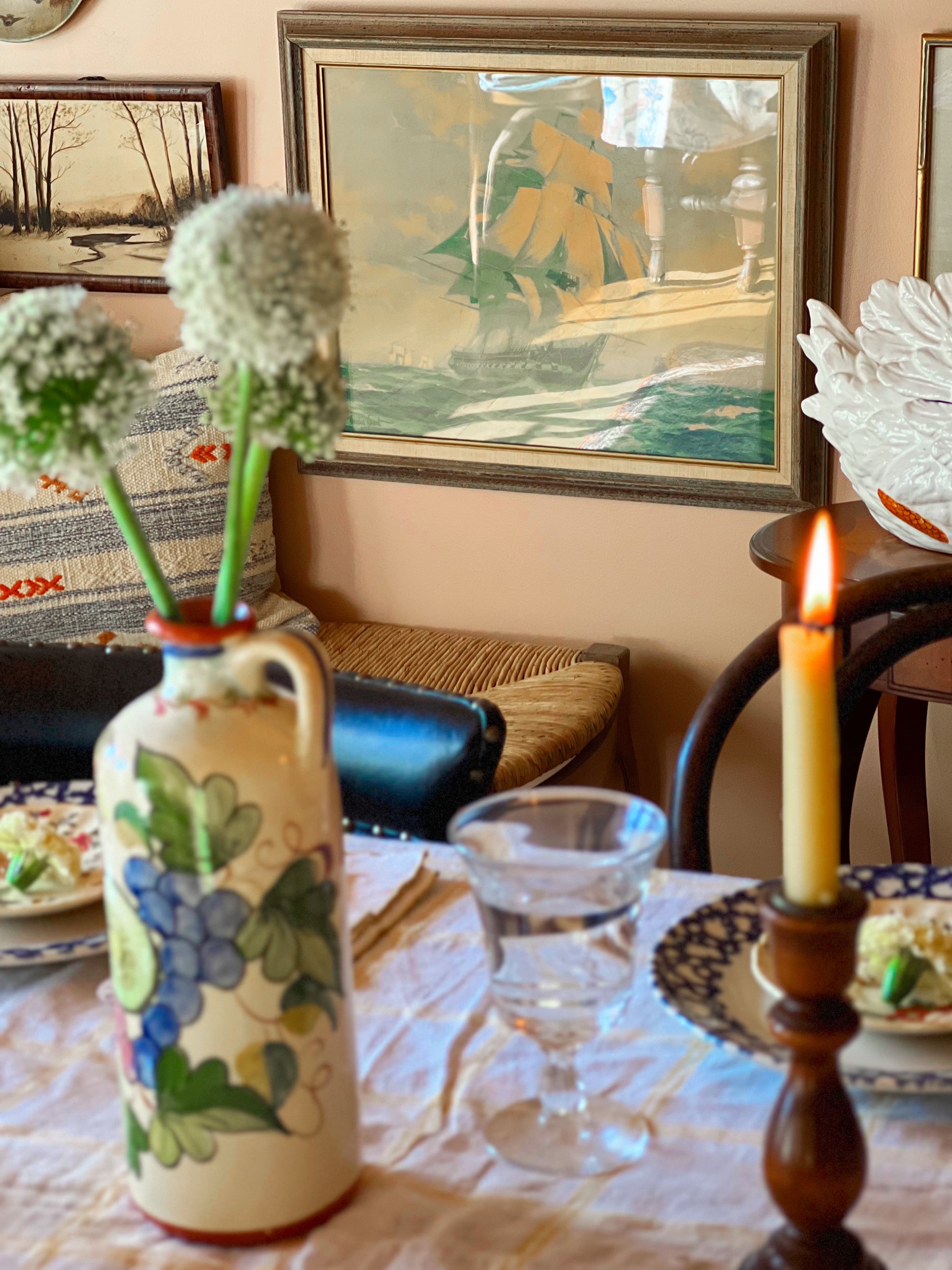 Decorative table setting with a vase, candle, and flowers in a room with framed artwork on the wall.