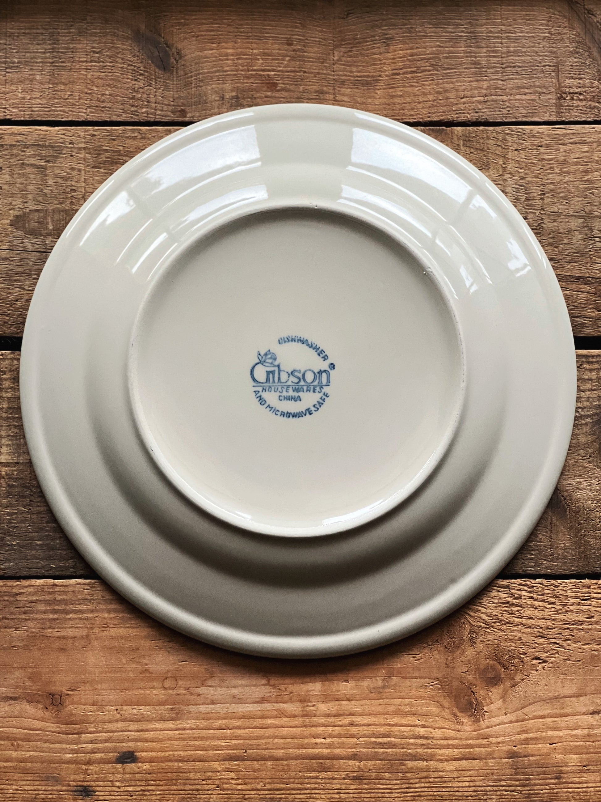 underside of a stoneware plate with 'Gibson' logo on a wooden surface