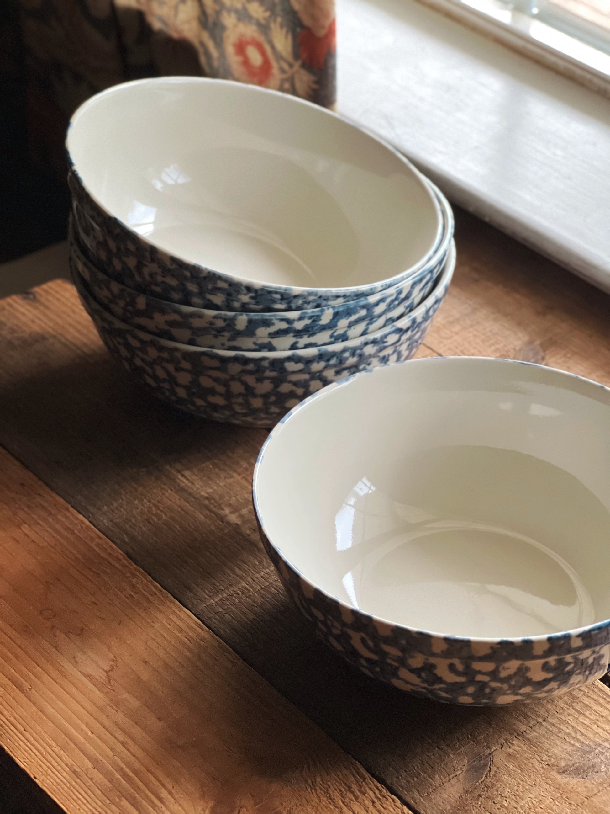 Stack of stoneware bowls with blue and white spongeware design on a wooden surface