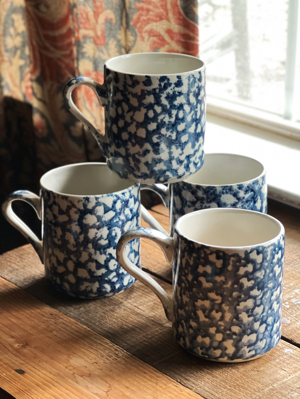 Set of blue and white spongeware mugs on a wooden surface with a window in the background.