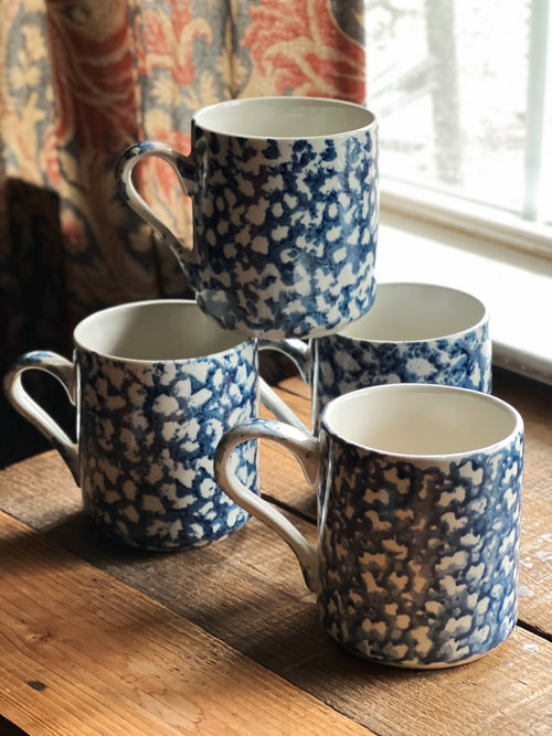 Set of blue and white spongeware mugs on a wooden surface with a window in the background.
