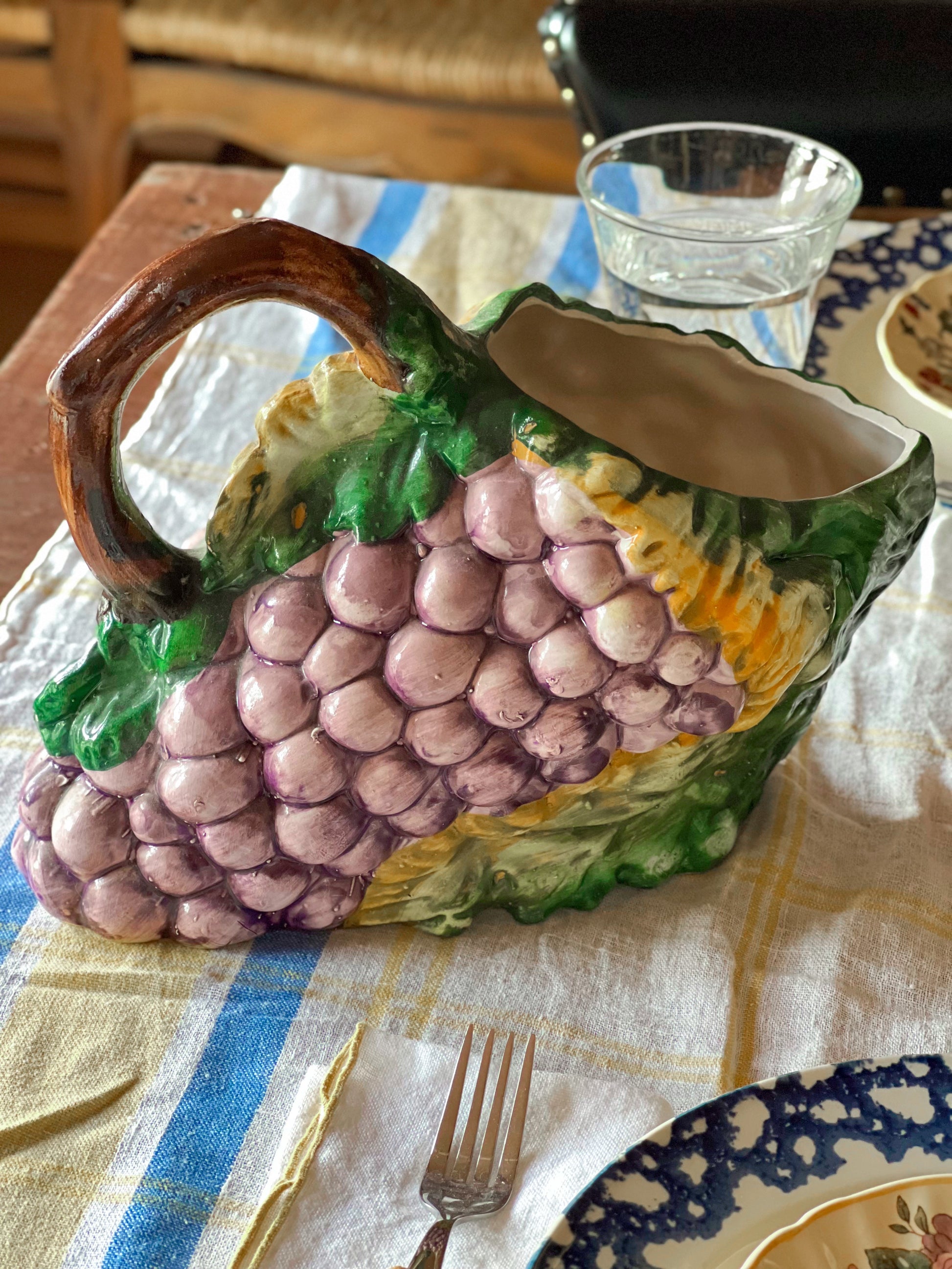 Decorative ceramic fruit pitchers shaped like a bunch of grapes on a tablecloth.