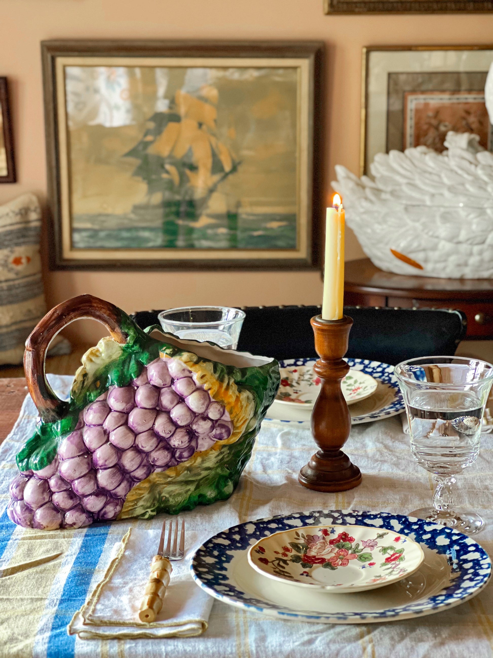 Decorative table setting with a ceramic grapevine piece, candle, and plates.