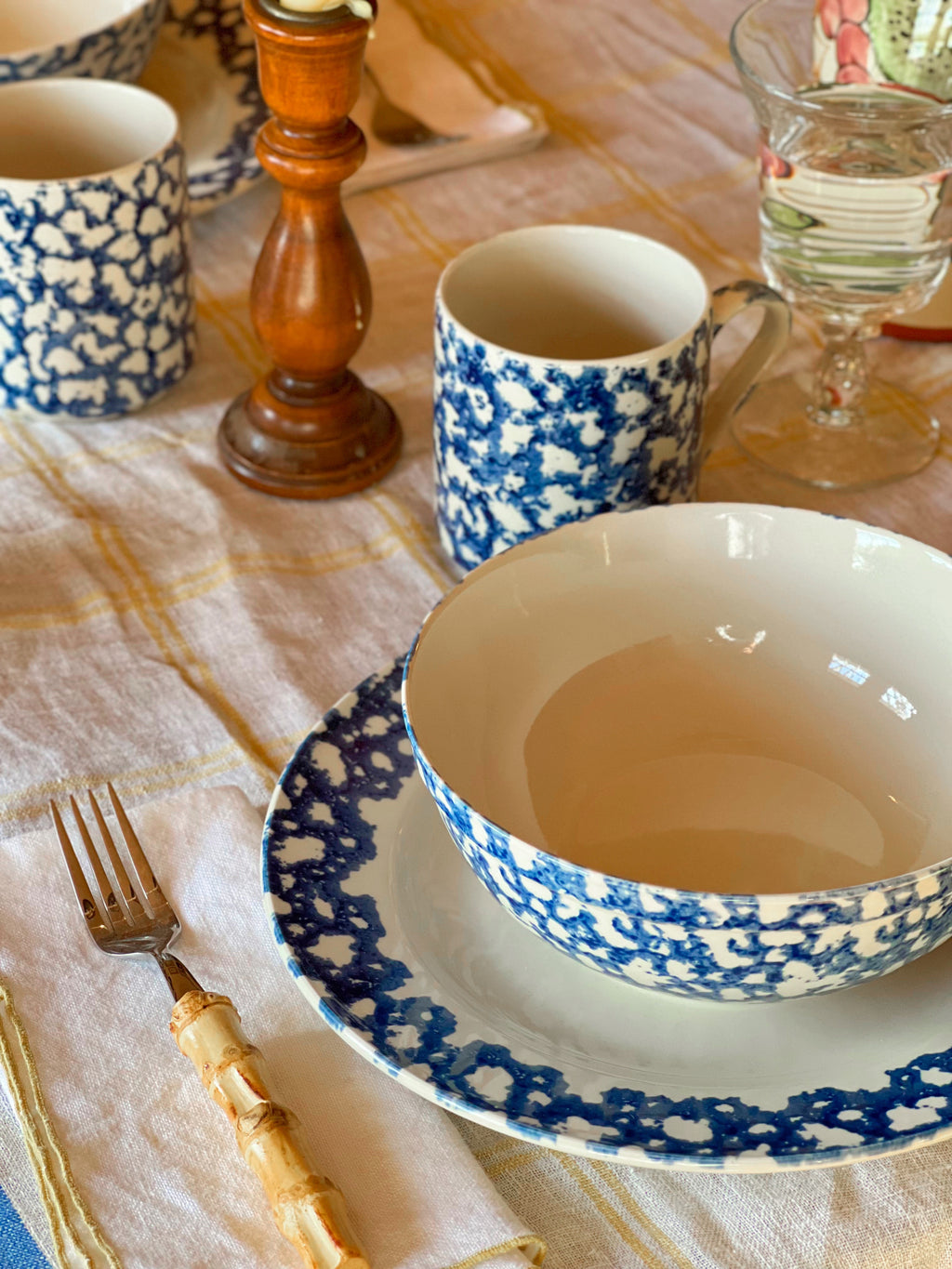 Dining table setting with blue and white spongeware cups and plates on a checkered tablecloth.