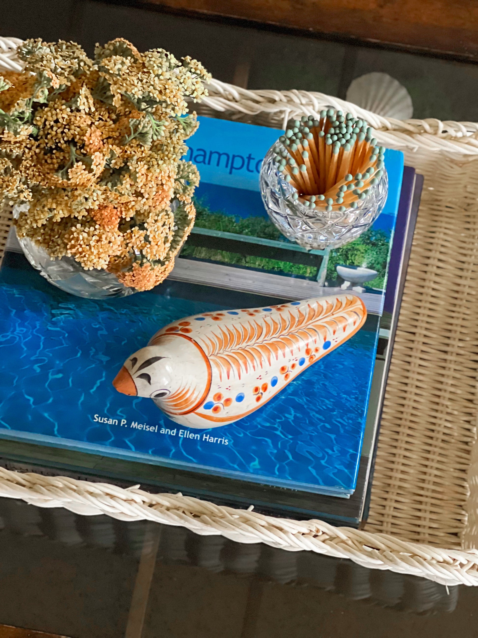Overhead view of a Tonala Mexico bird figurine on a book with wicker surface and blurred background