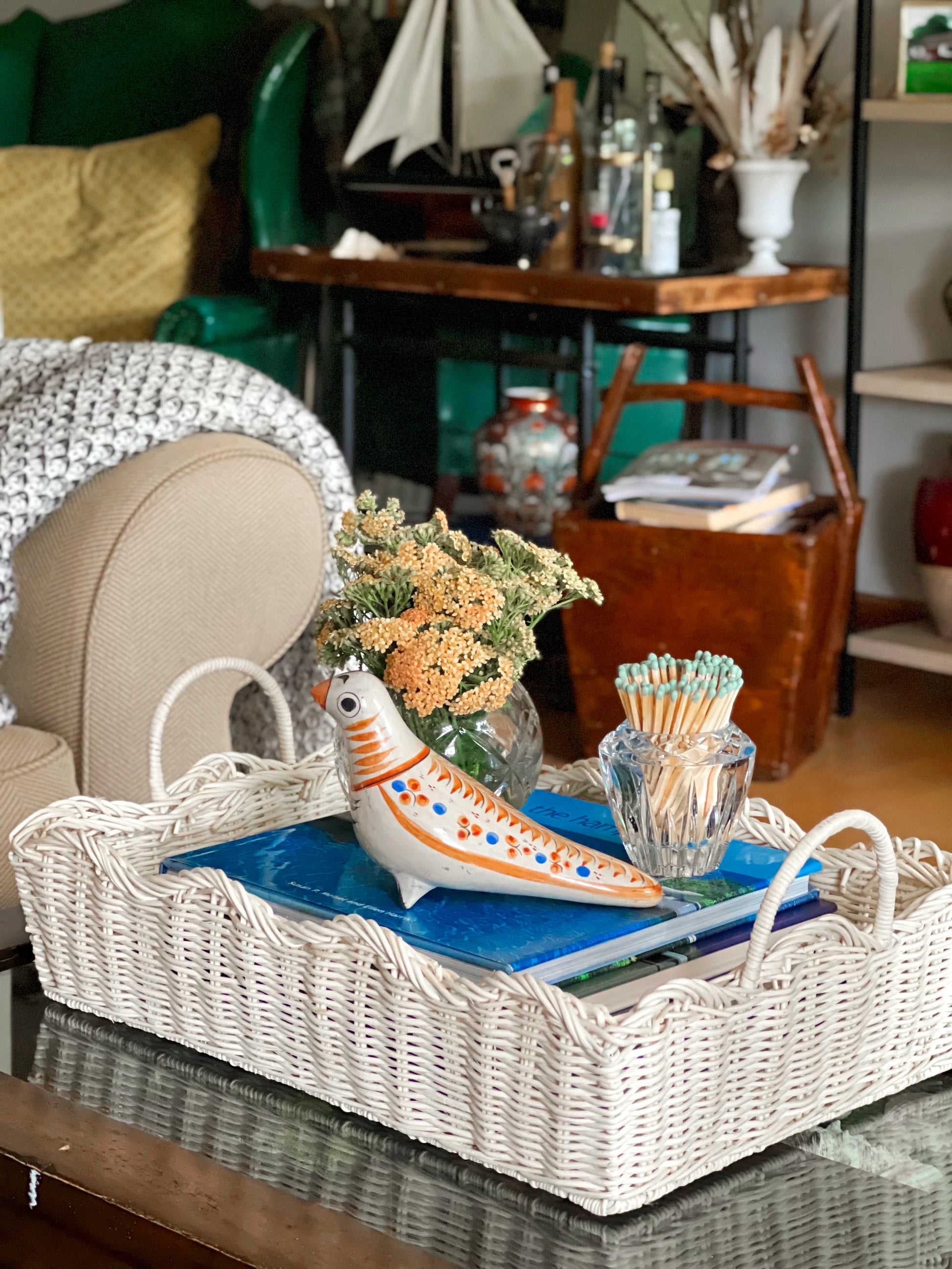 Decorative tray with a ceramic bird, flowers, and books on a table in a living room.