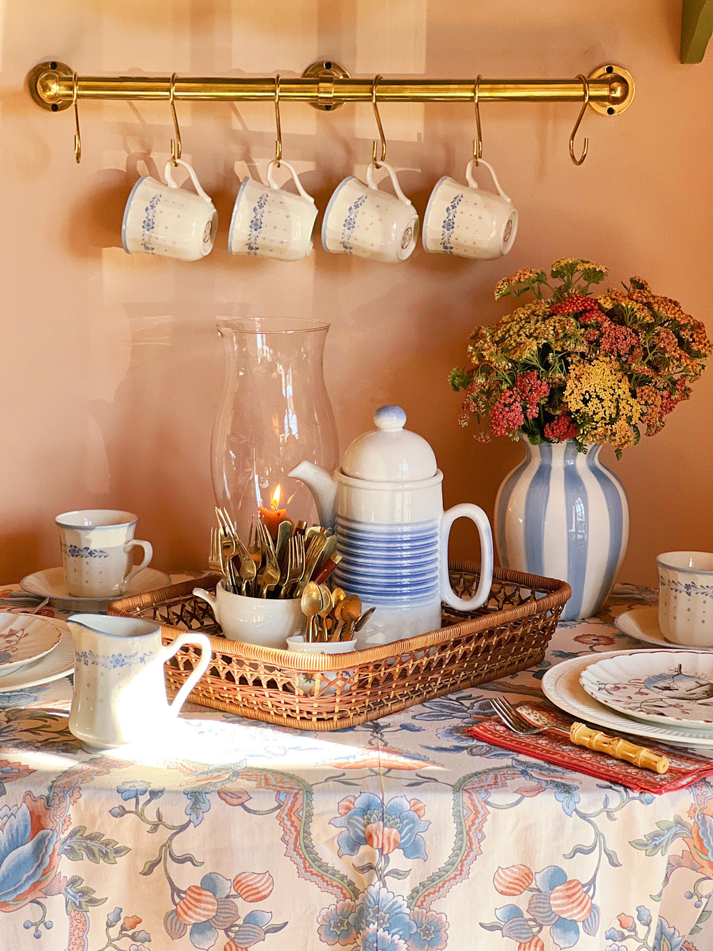 Café setting with mugs, teapot, and floral arrangement on a table.