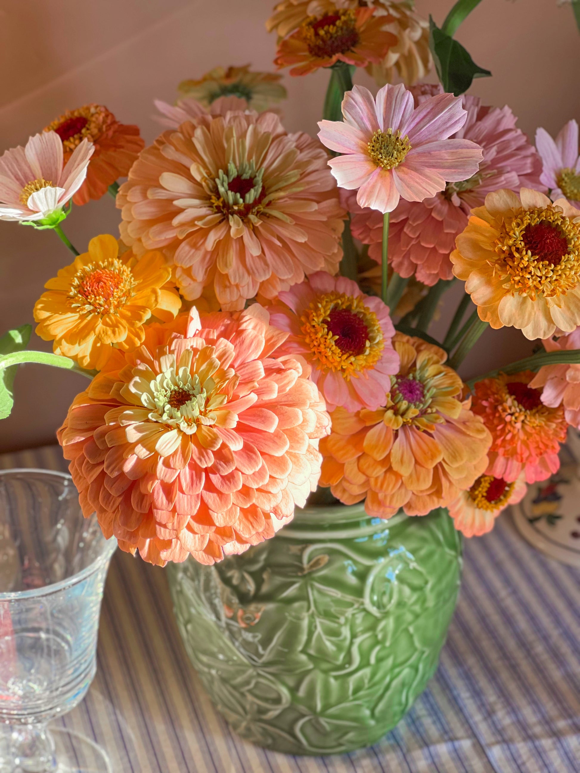Colorful flowers in a green vase on a table with a striped tablecloth.