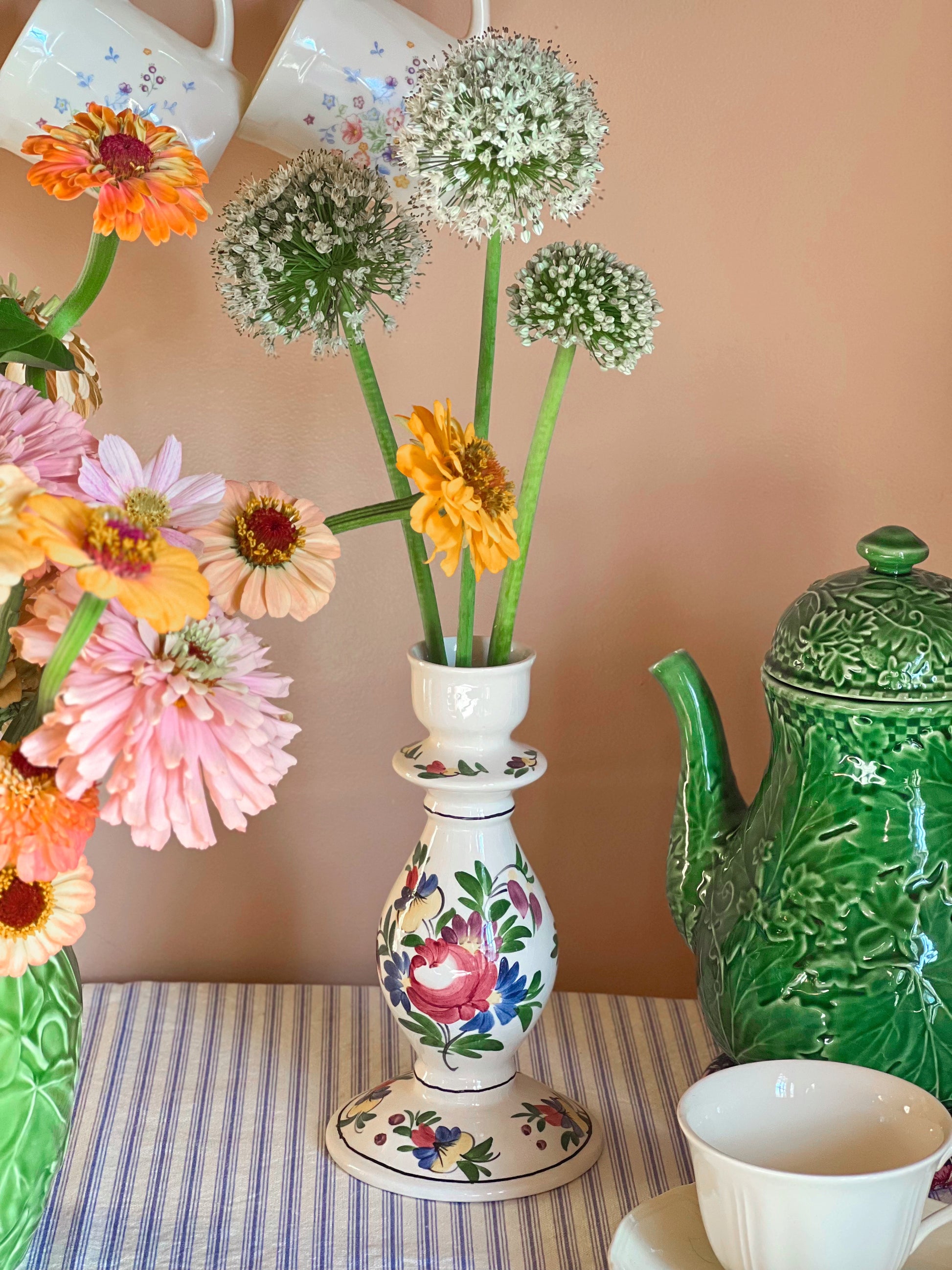 Decorative floral arrangement in a colorful vase on a table with a green teapot and striped cloth.