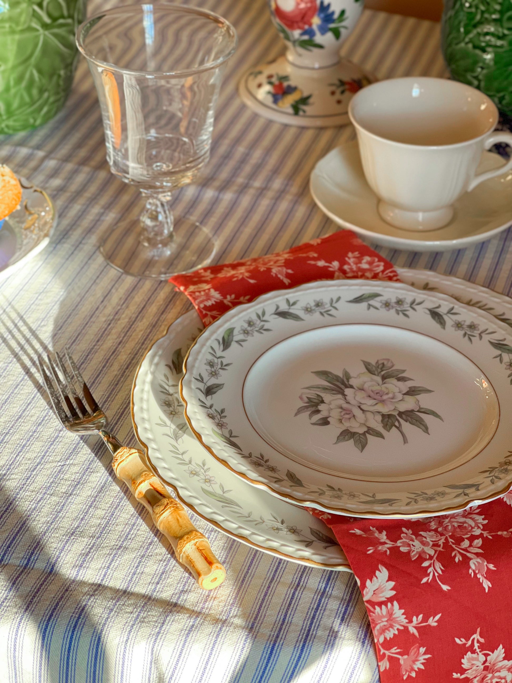 Set table with floral plates, a Wedgwood Queen's shape teacup and saucer set, and a striped tablecloth.