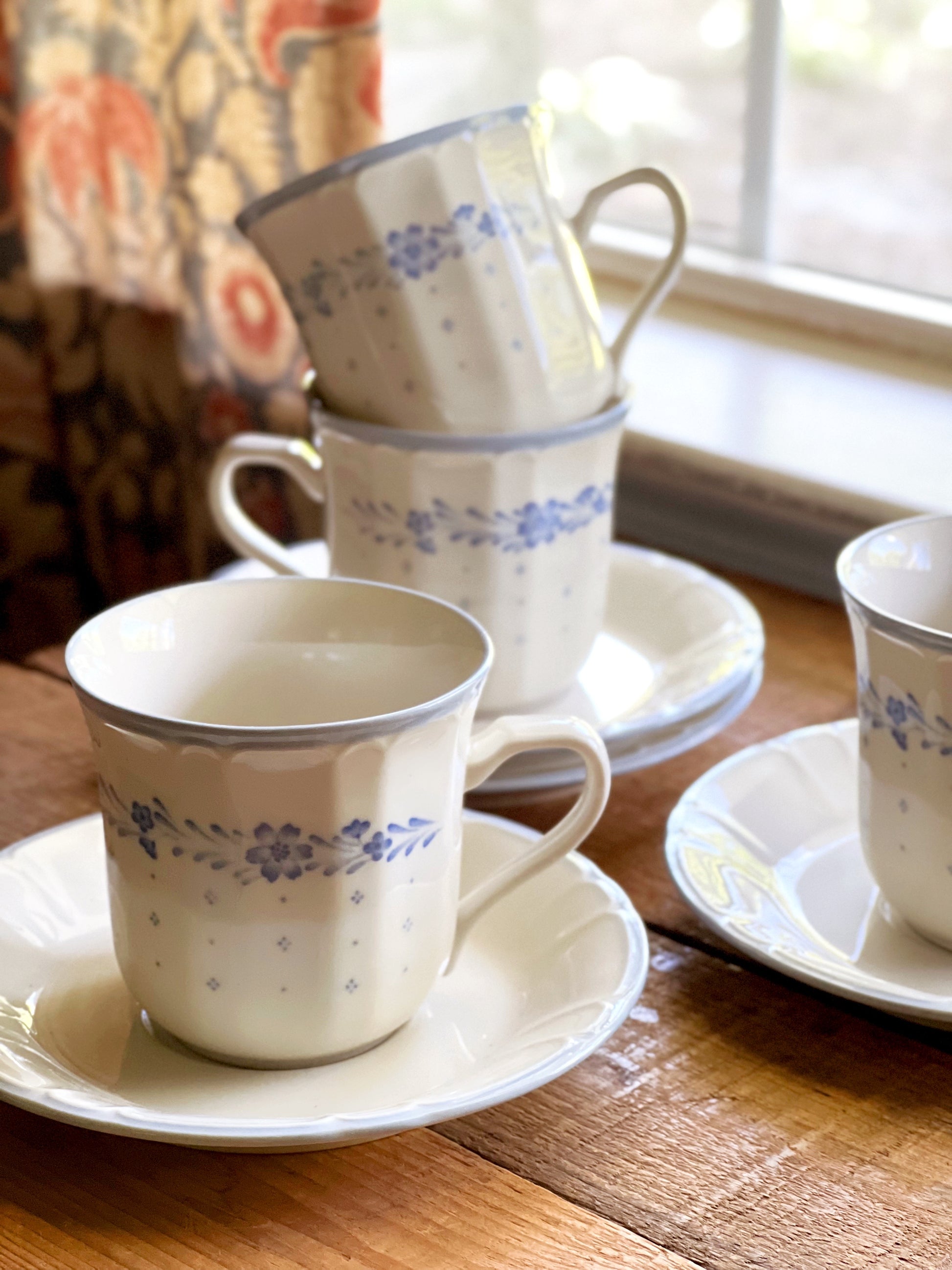 Set of ceramic cups and saucers with floral patterns on a wooden table.
