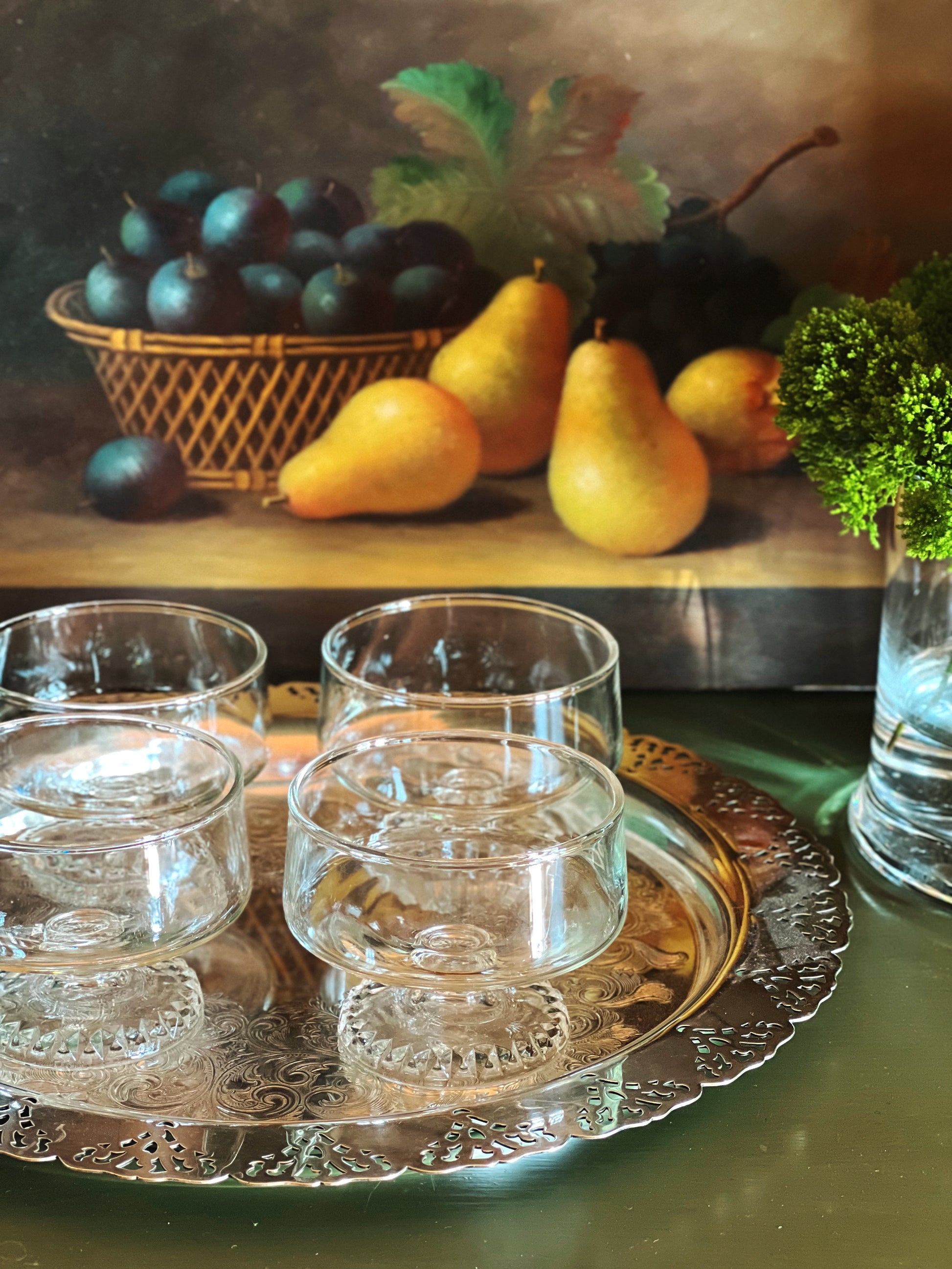 Vintage coupe glasses displayed on a silver tray with pears and dark grapes in the background.