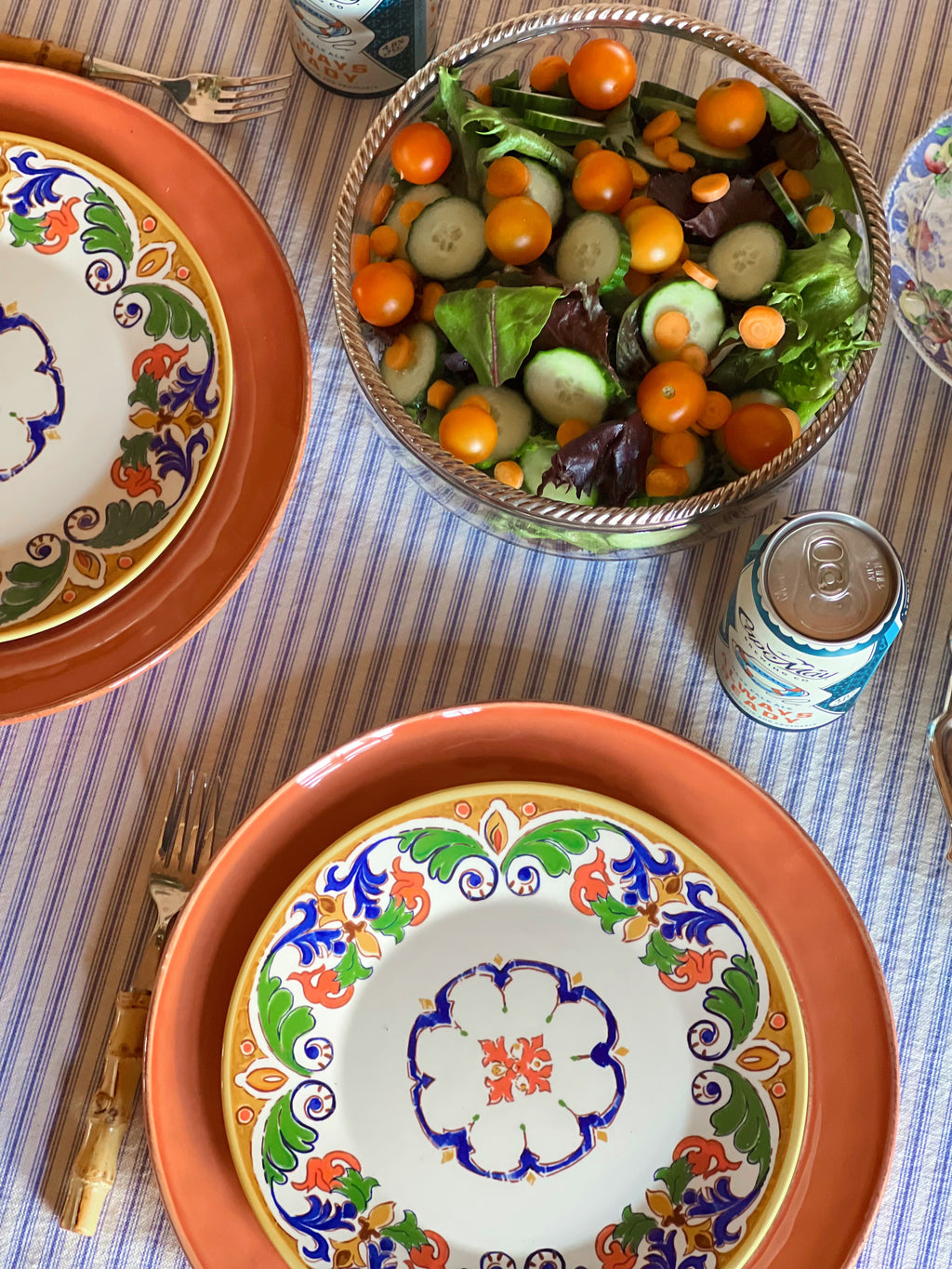 Decorative plates with colorful patterns on a table with a salad and drinks.
