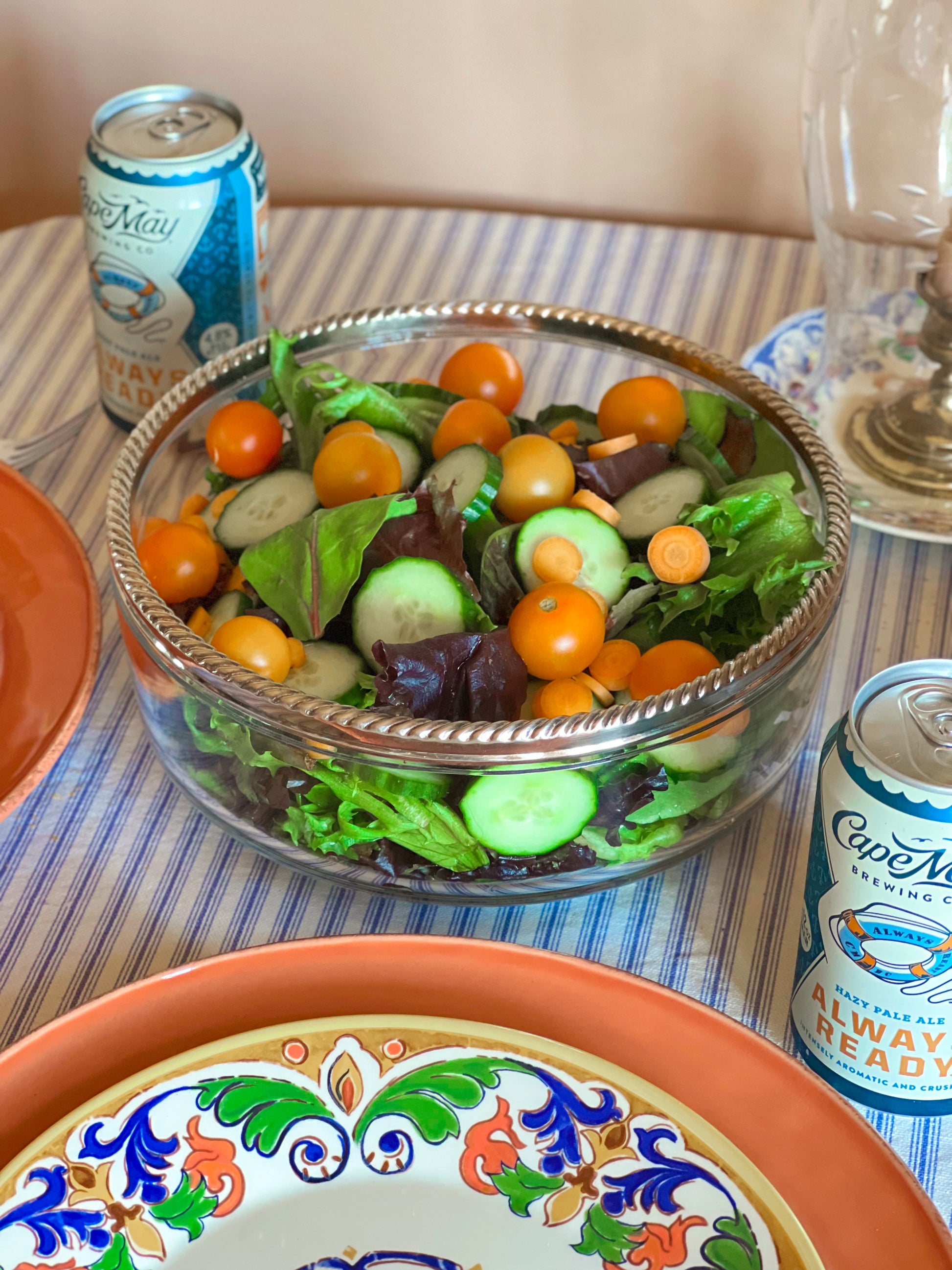 Salad in a glass bowl with cherry tomatoes and cucumbers, served on a table with Cape May beer cans.