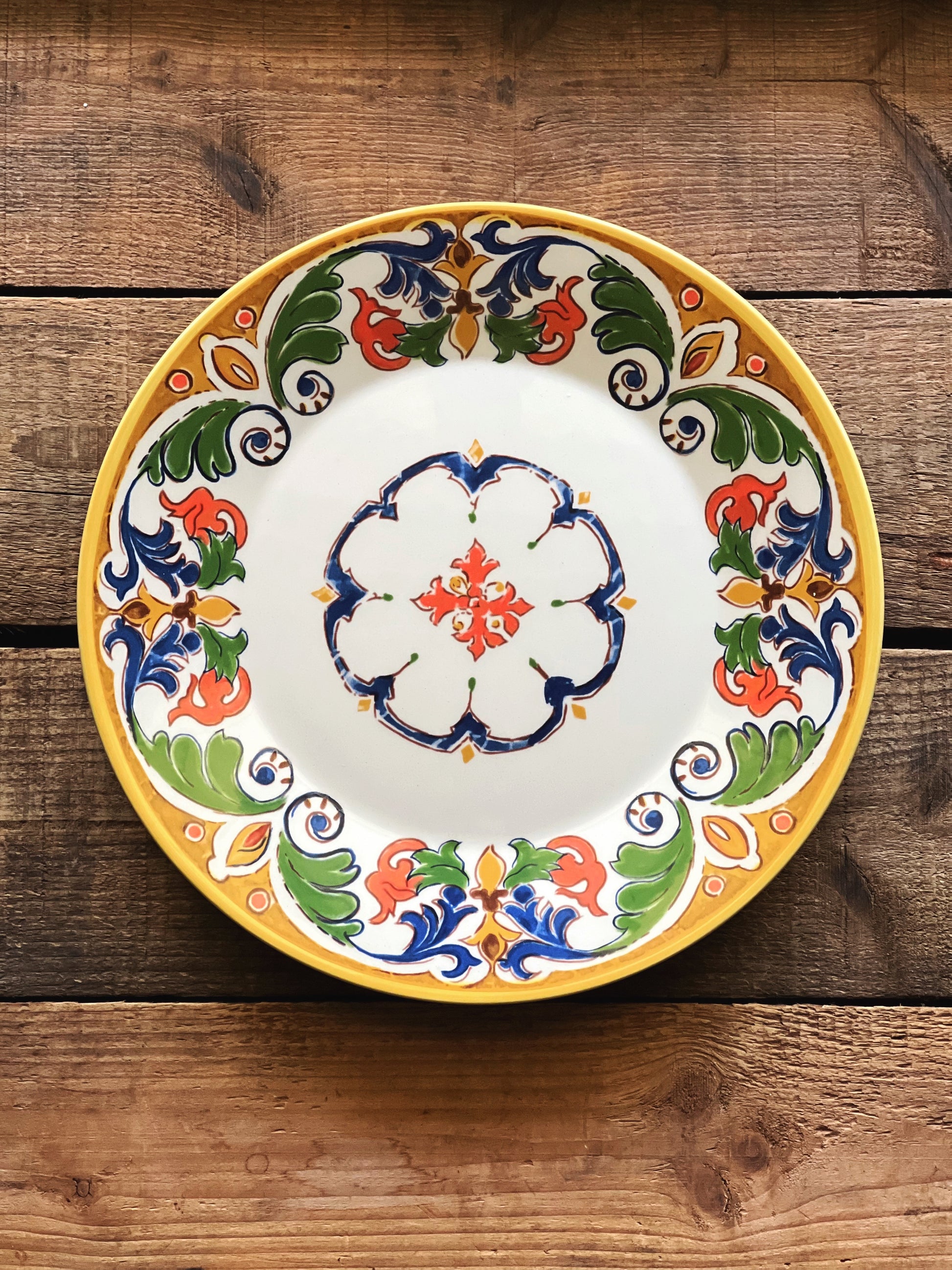 Colorful CMG Portugal ceramic luncheon plate featuring a Mediterranean-inspired floral motif and terracotta border on a rustic wood table.