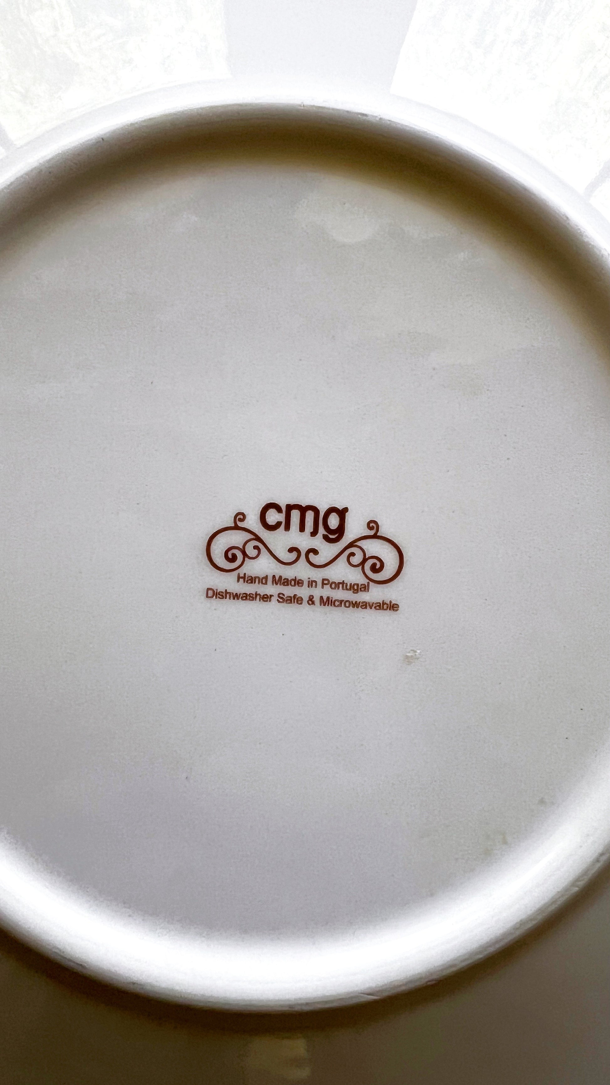 Close-up of a ceramic plate with 'cmg' branding on a white background