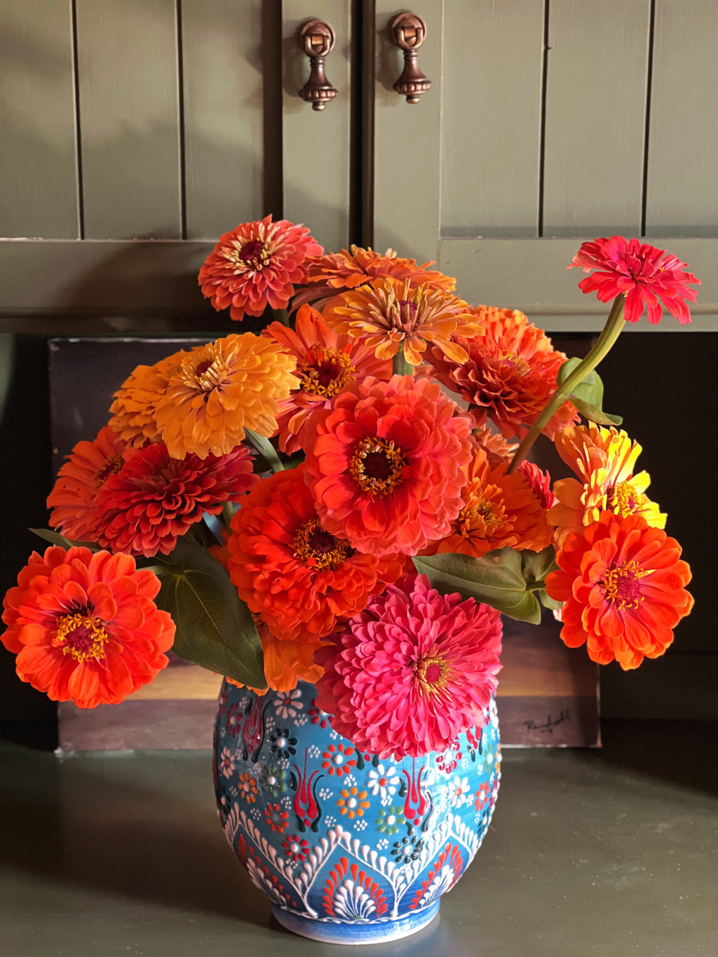 Vintage hand-painted ceramic vase with raised floral decoration and scalloped rim filled with colorful zinnias in warm natural light.