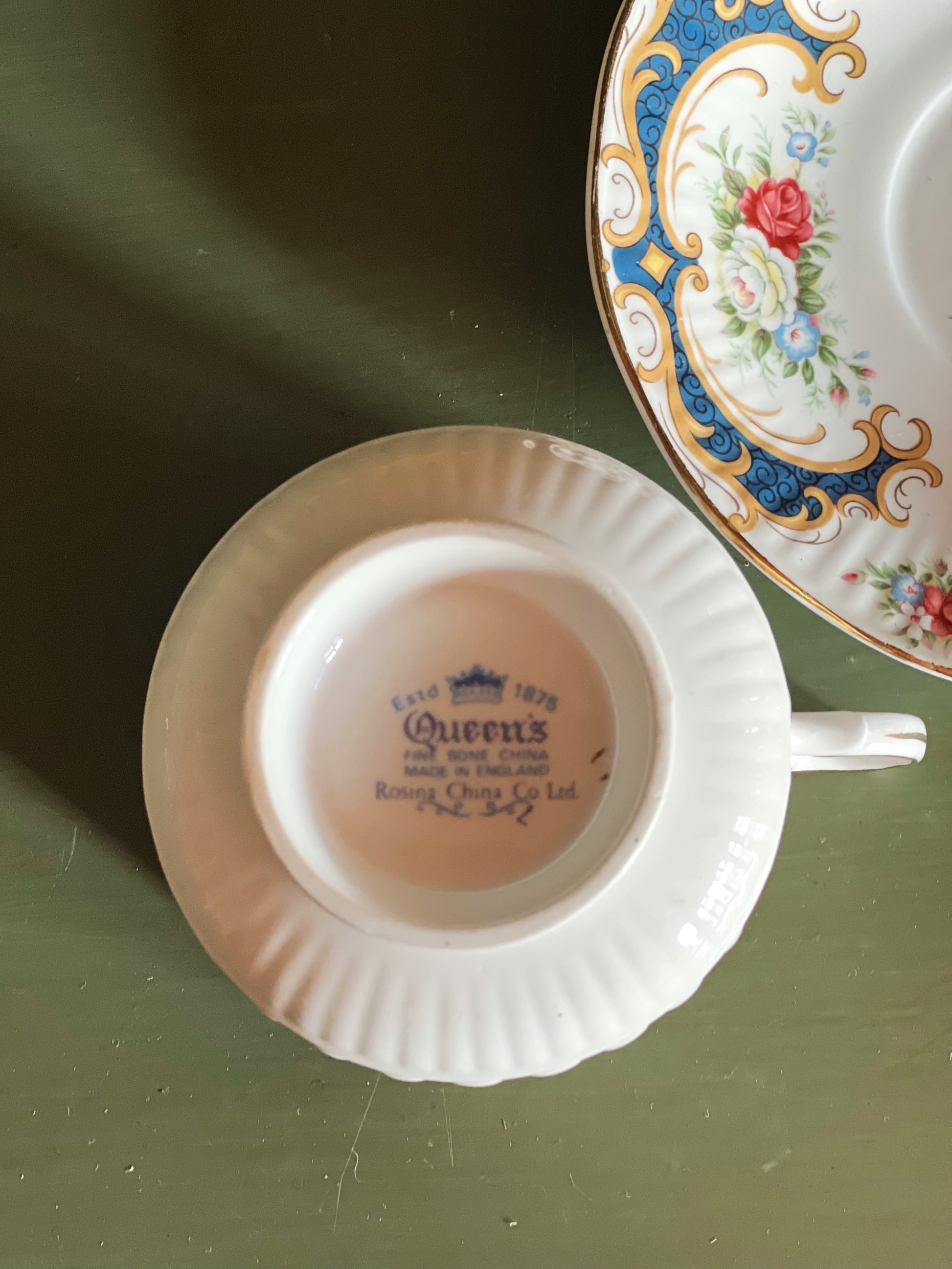 Teacup with 'Queen's' branding on a green surface