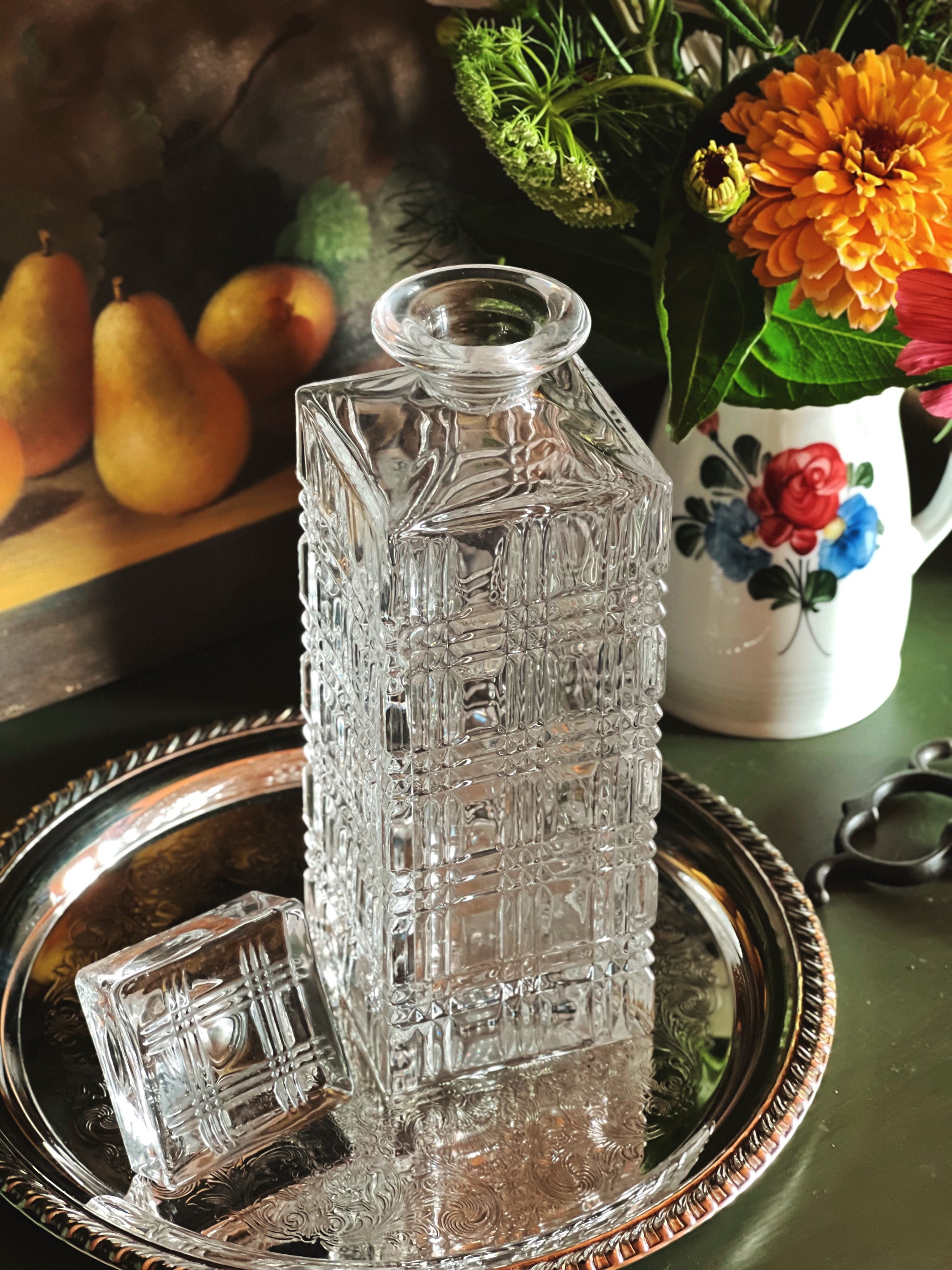 Clear glass decanter on a decorative tray with pears and flowers in the background