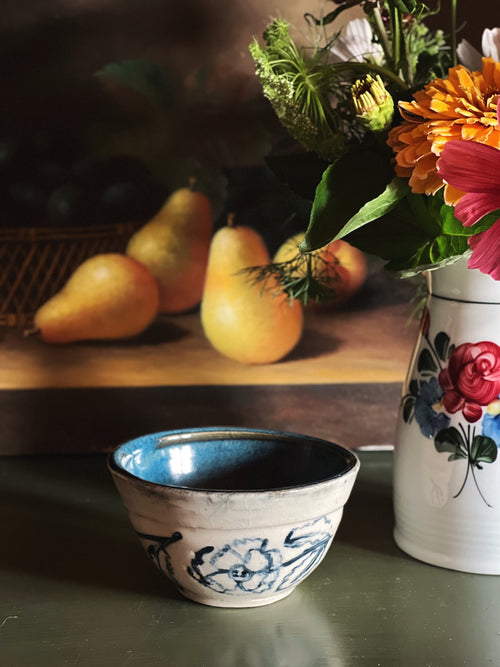 Handmade Blue Floral Pottery Bowl next to a still life painting and a flower arrangement