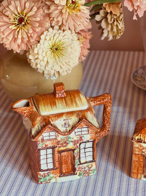 Vintage Price Bros Ye Olde Cottage teapot made in England with hand-painted thatched roof cottage design, photographed with fresh garden flowers in warm natural light.
