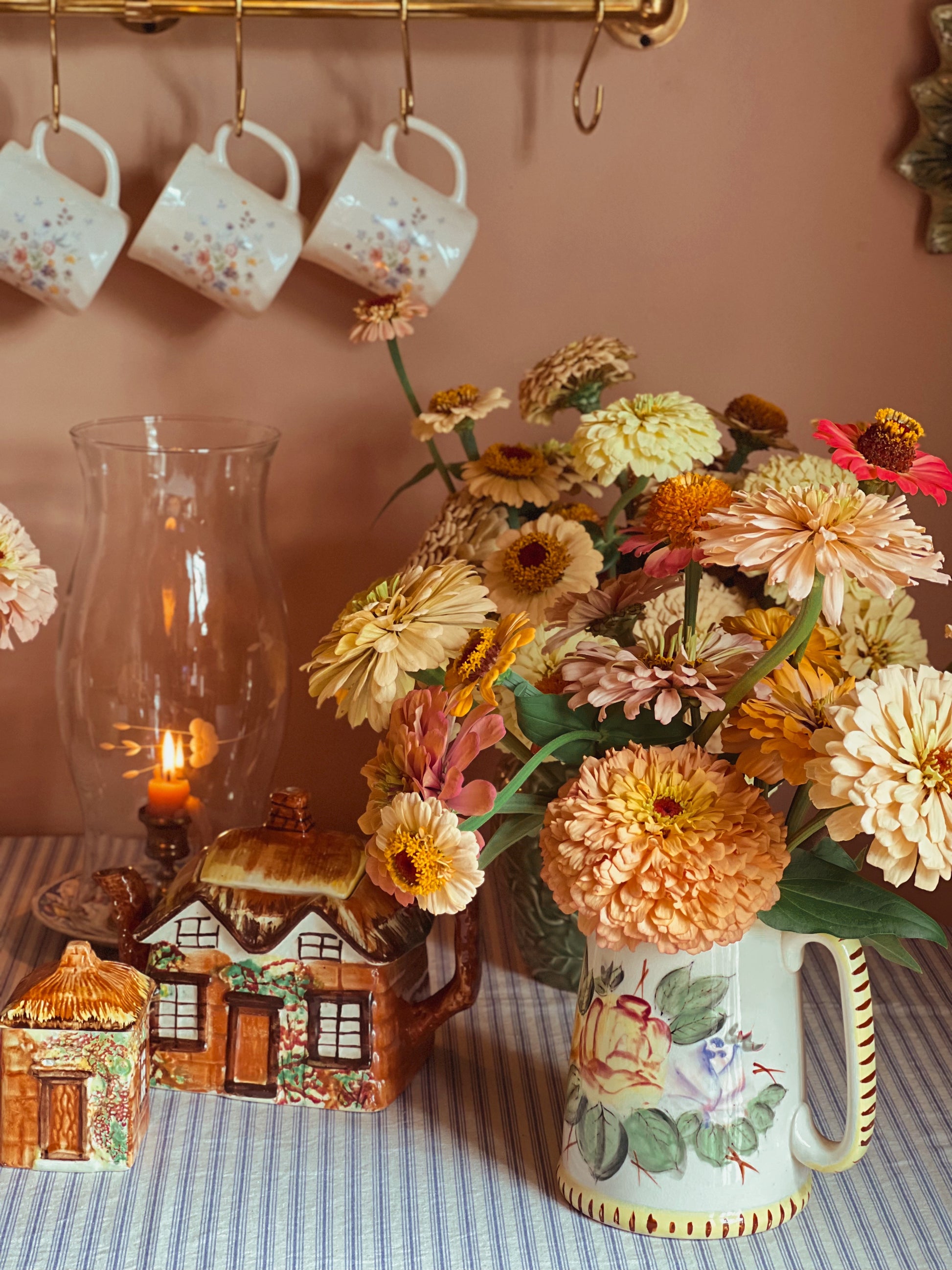 Decorative table setting with flowers, mugs, and small houses against a pink wall.