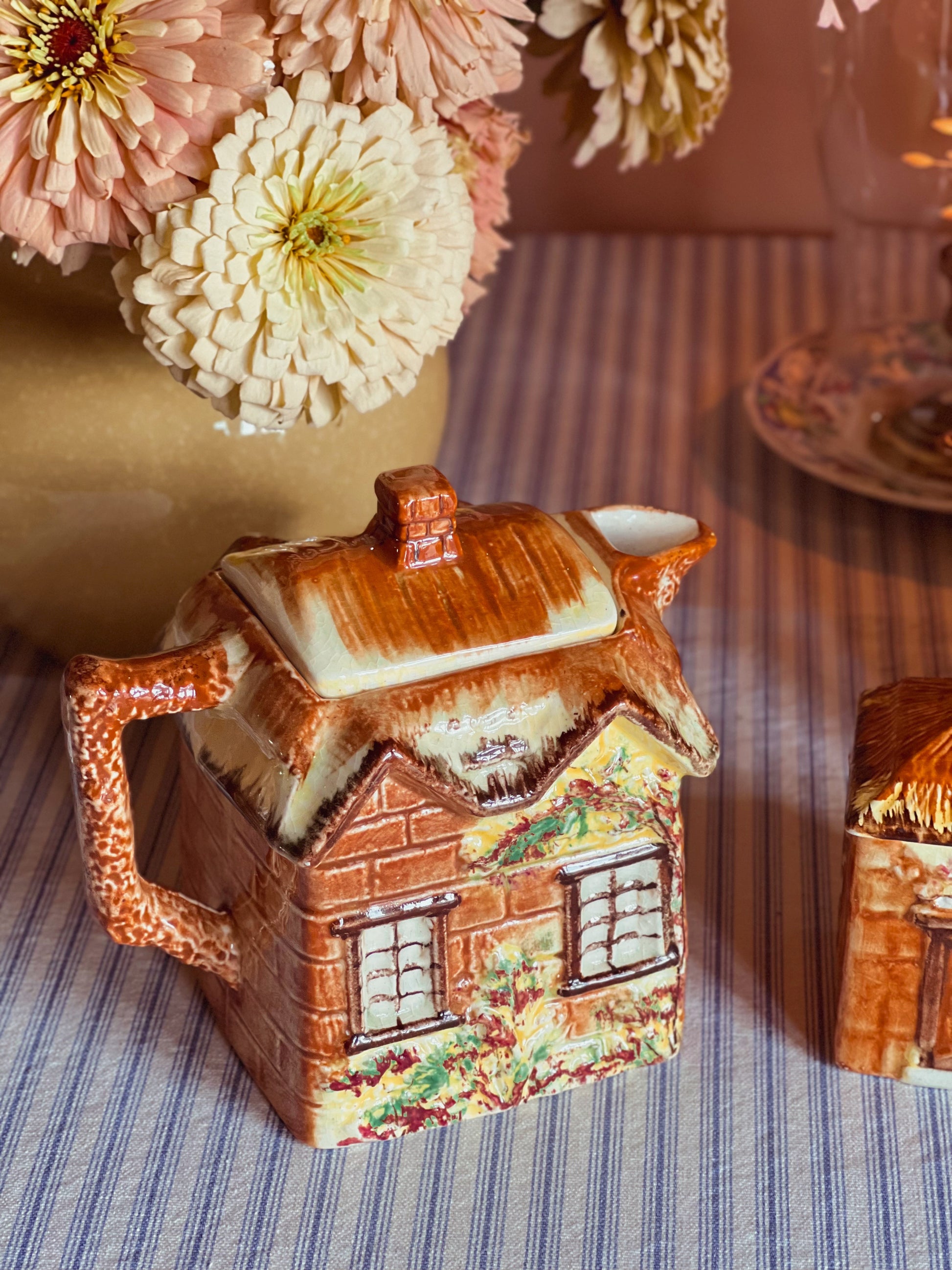 Backside of a vintage Price Bros Ye Olde Cottage teapot made in England with hand-painted thatched roof cottage design, photographed with fresh garden flowers in warm natural light.