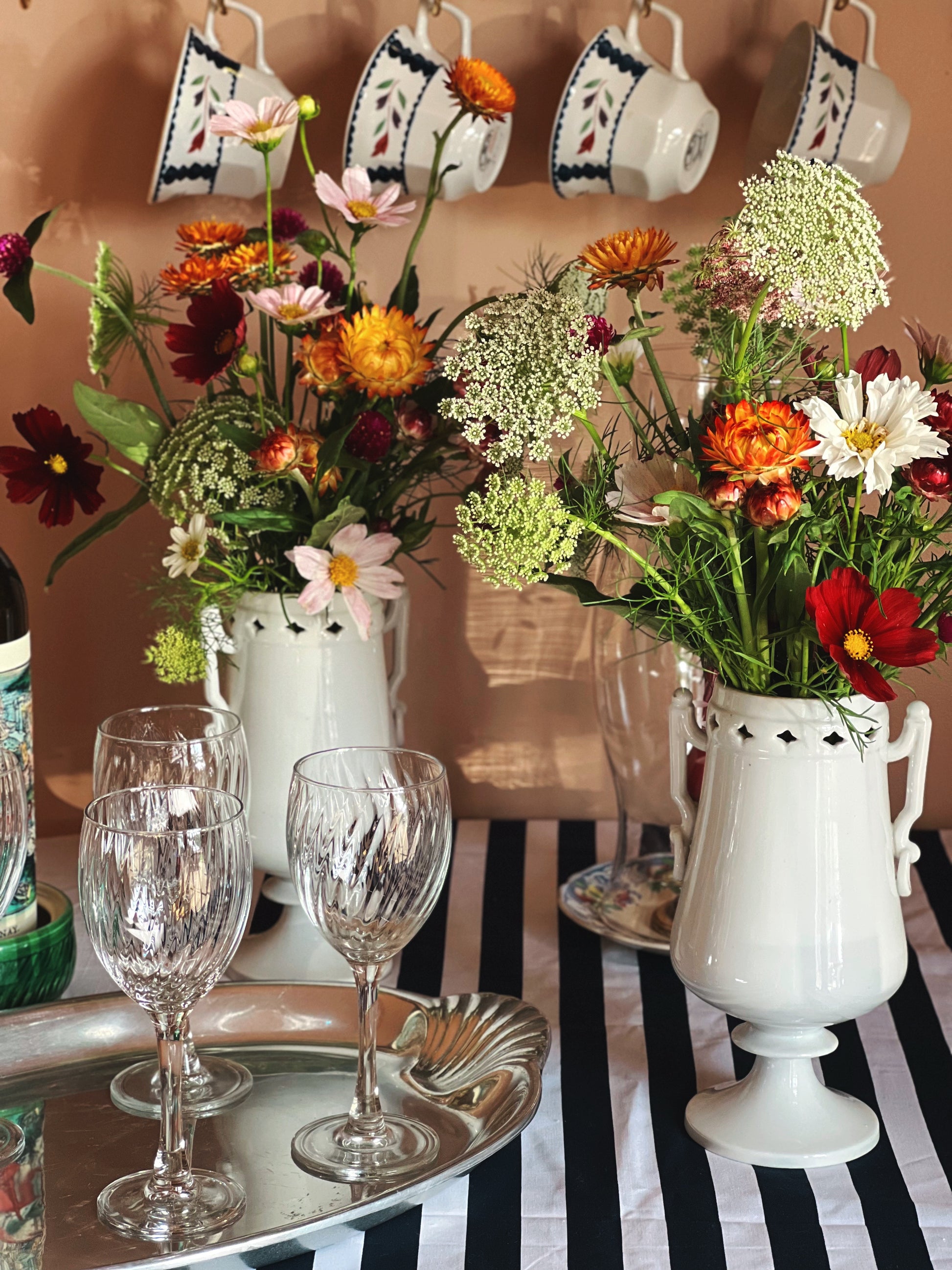 Vintage white porcelain urn vase with sculptural handles filled with fresh garden flowers on a striped table.