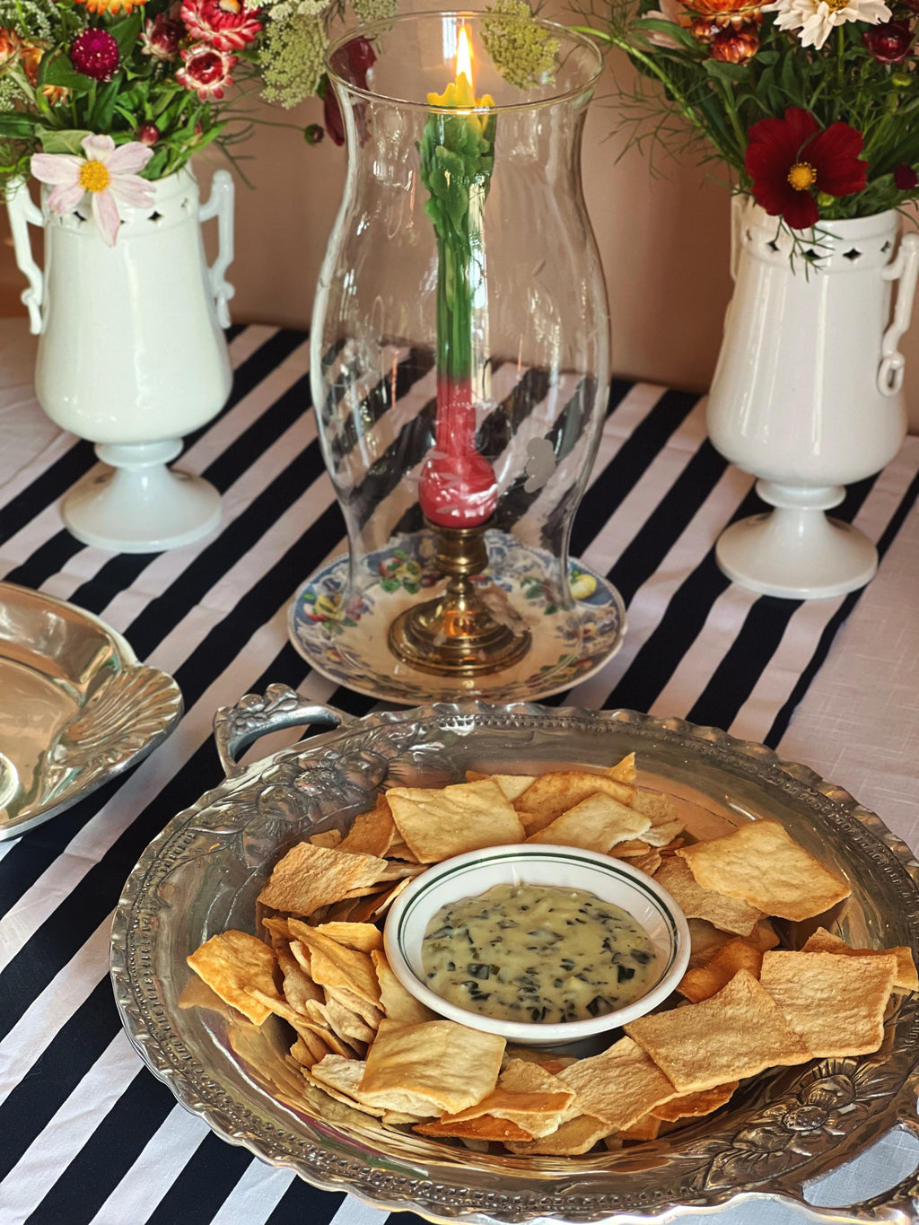 Vintage embossed silver serving tray with decorative fruit border and double handles on a table with a striped tablecloth.