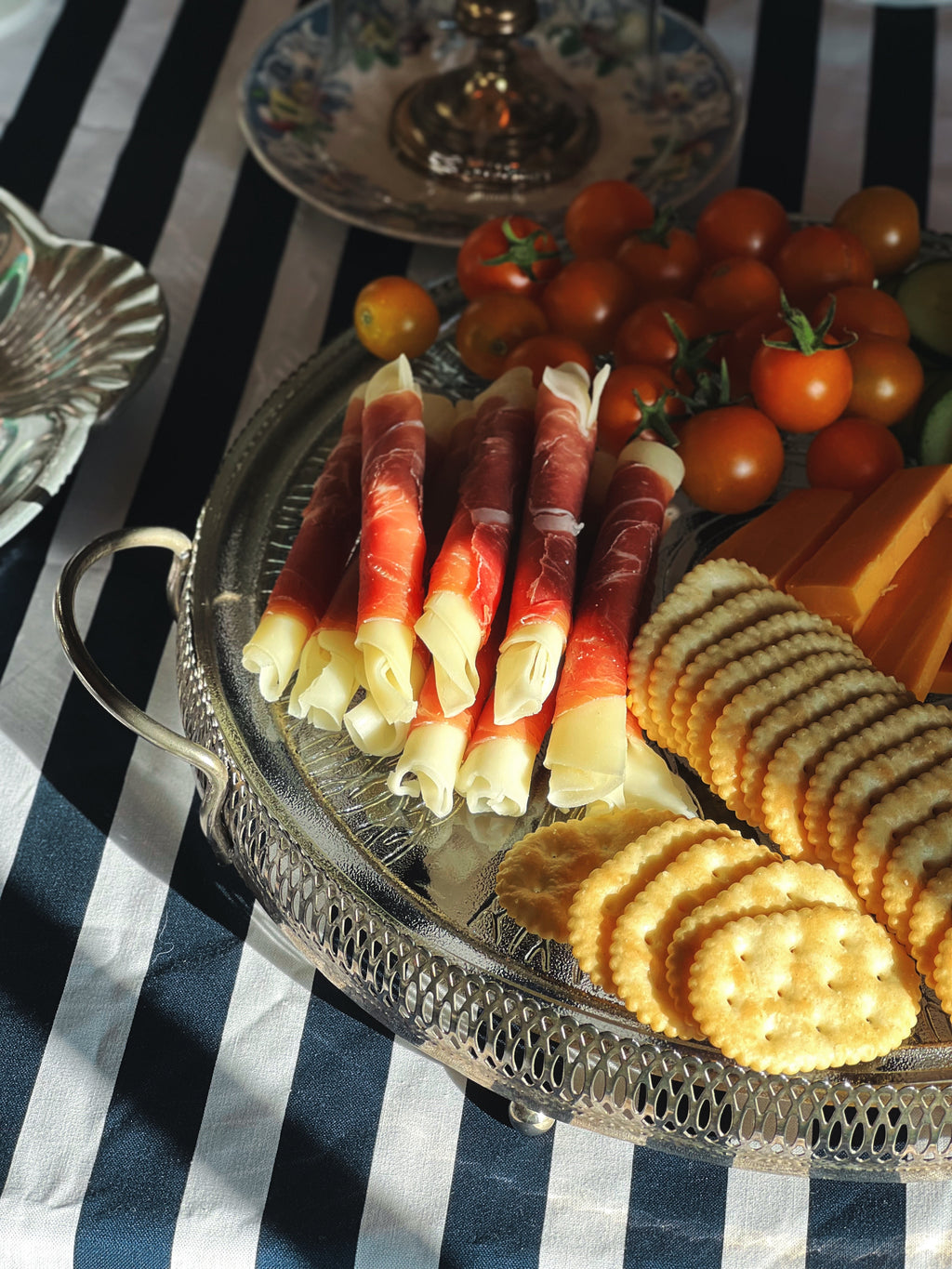Vintage frosted swirl glass serving platter in a silver footed stand styled with charcuterie, crackers, cheese, grapes, and tomatoes.